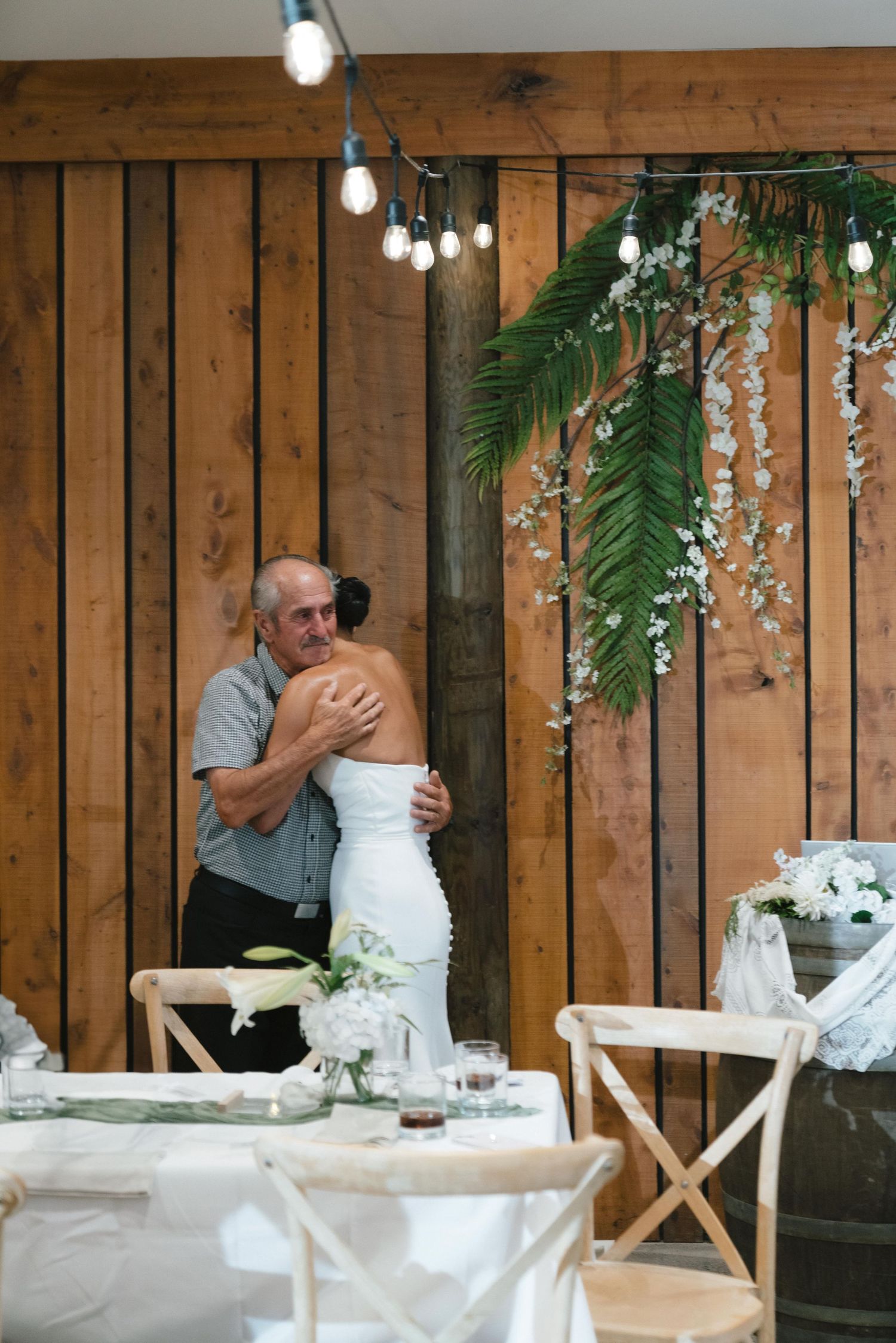 Indoor wedding celebration with wooden paneled walls and hanging greenery decor.