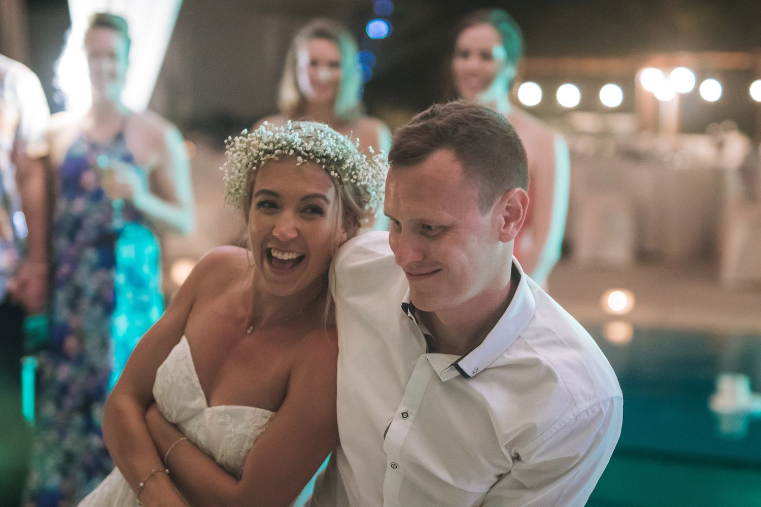 Dancing couple sharing joyful moment at reception with teal lighting and festive atmosphere.