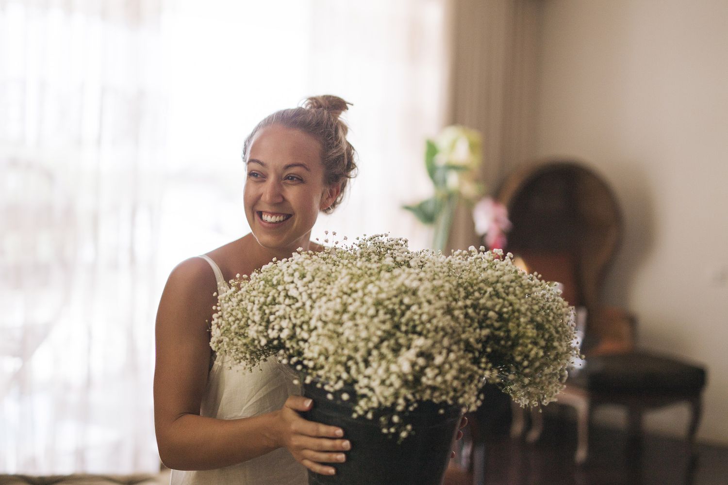 Joyful person laughs while holding large bouquet of baby's breath flowers in a bright interior room.