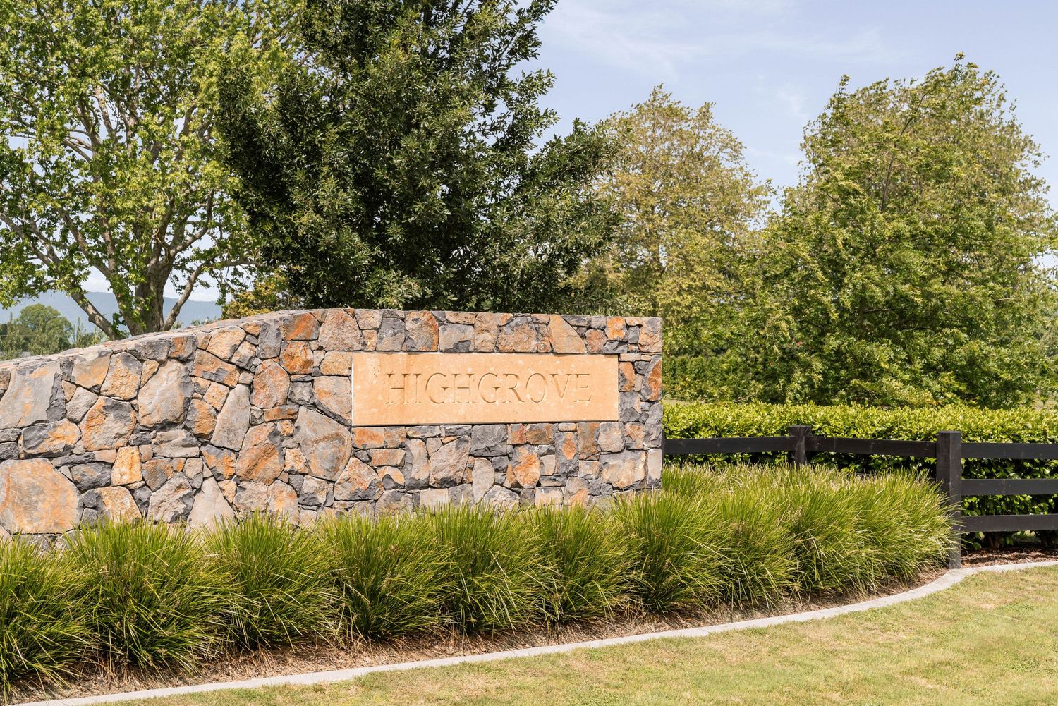 Close-up of a rustic stone wall entrance feature with ornamental grasses and landscaping.