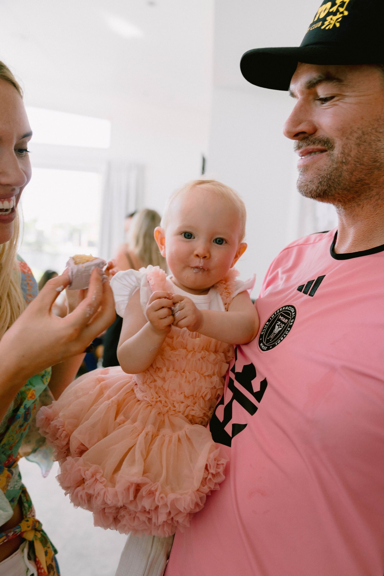 Baby in a pink tulle dress being held during a birthday celebration.