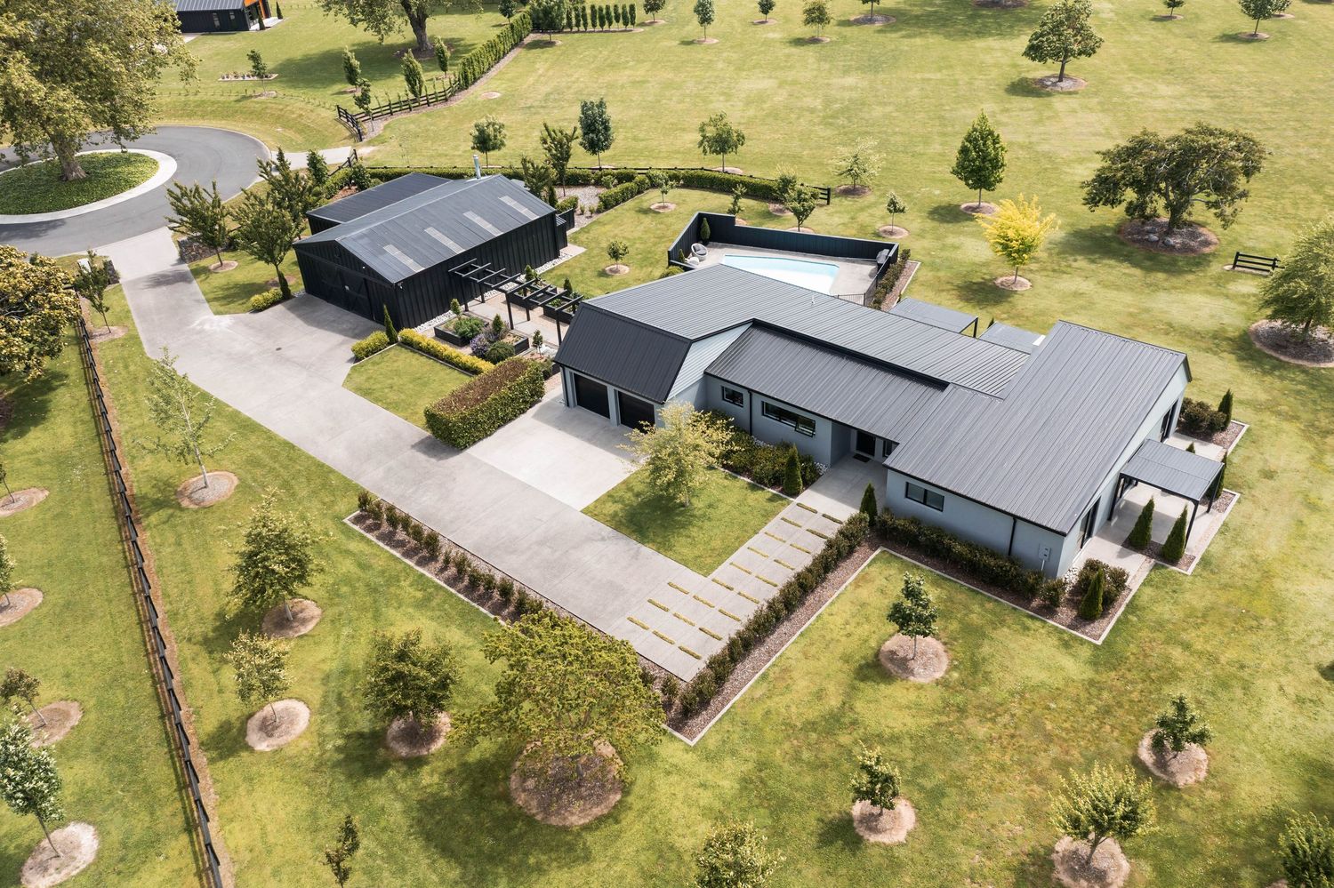 Aerial view of a modern house with black roof and white exterior walls situated on a spacious green property.