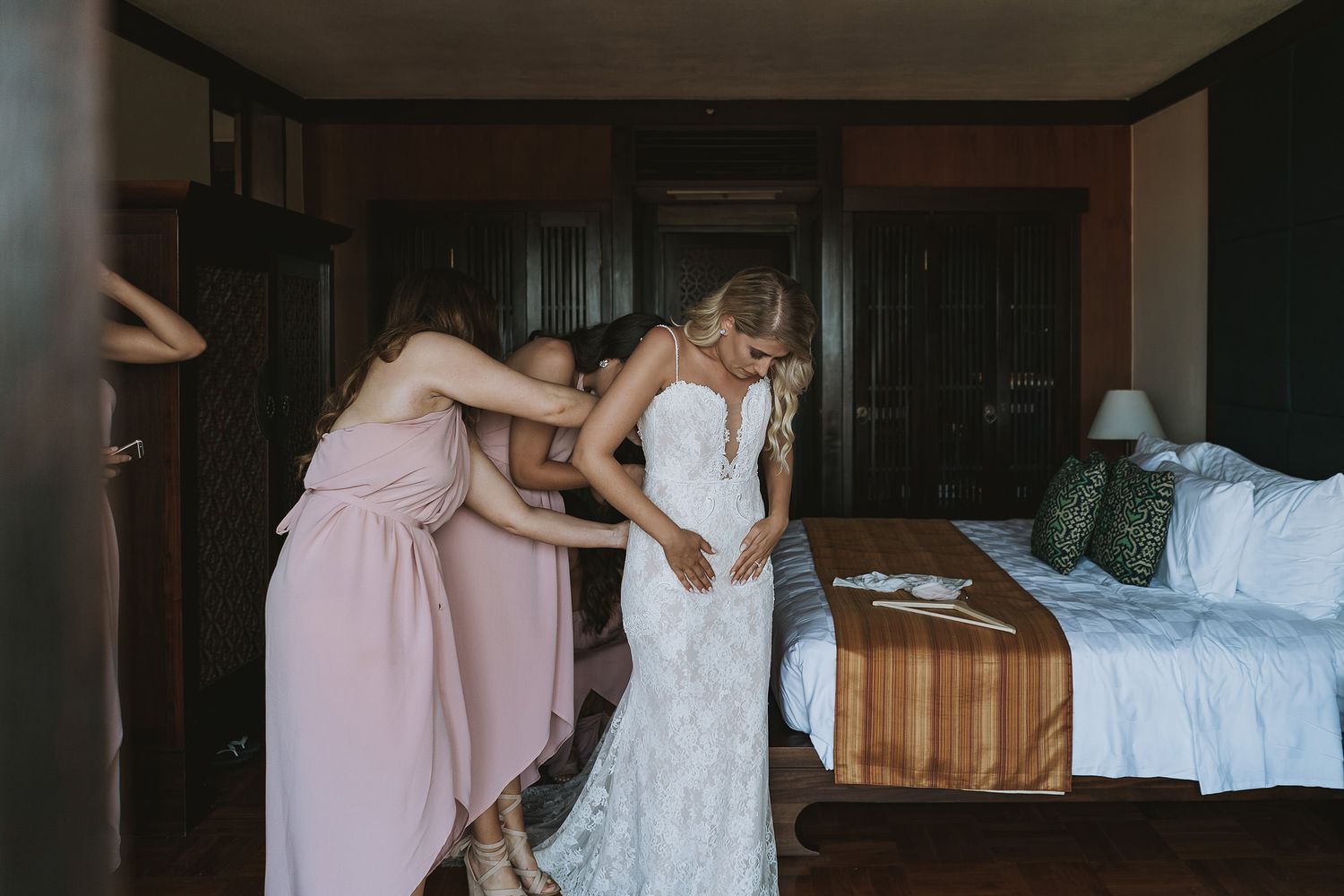 Wedding preparations in a hotel room as white lace dress is being fitted.