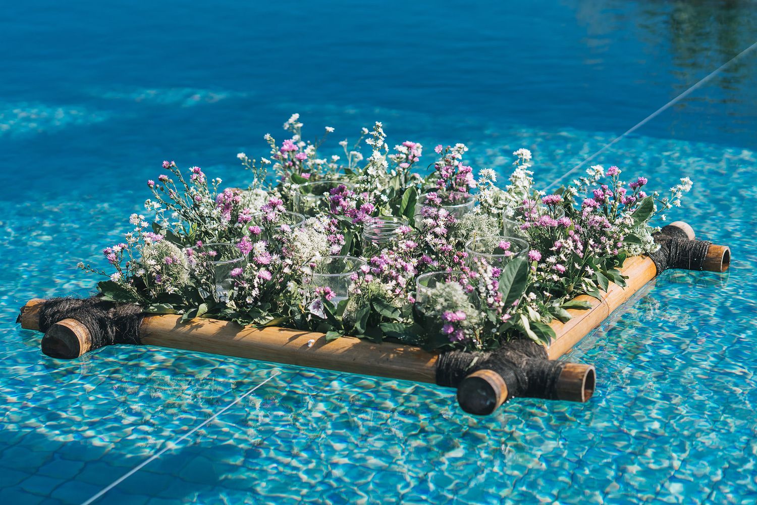 Small pink and white flowers growing in a wooden planter float on bright blue pool water.