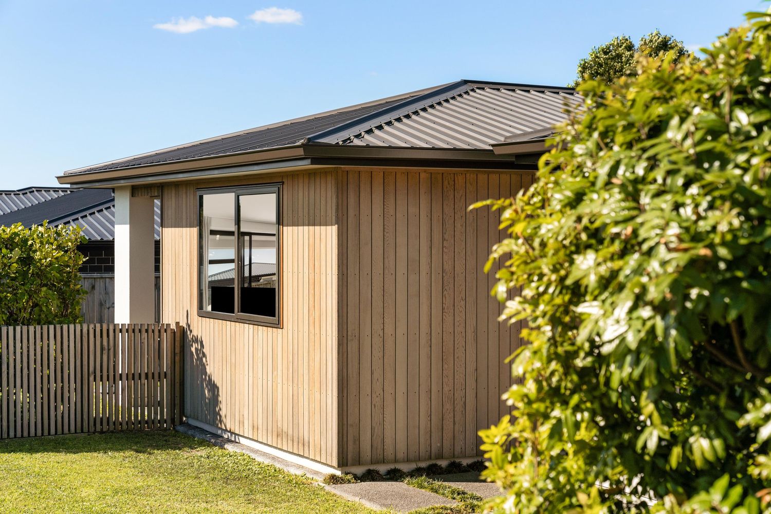Modern light brown timber house exterior with corner view showcasing landscaping and manicured garden.