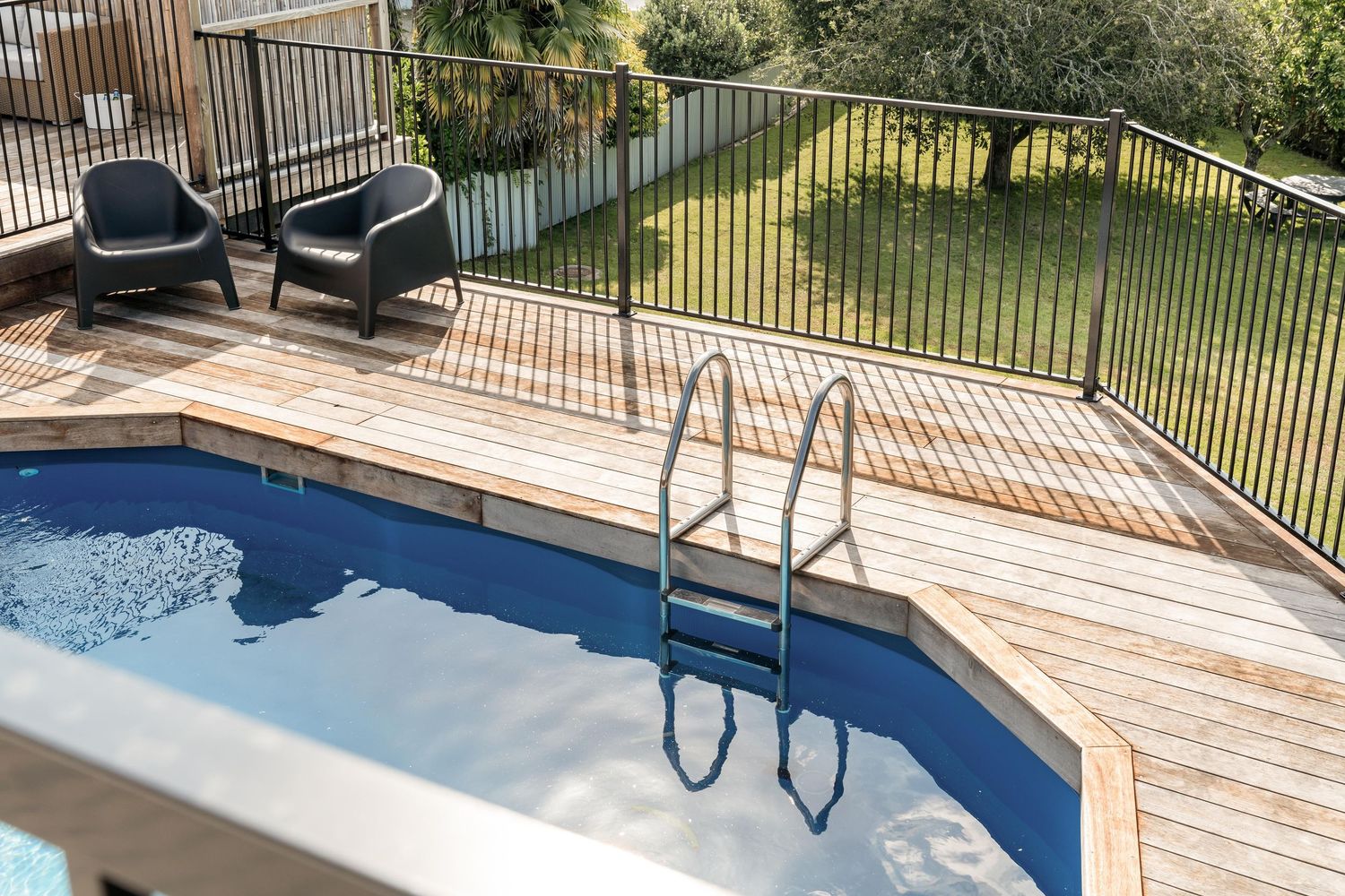 Swimming pool with wooden deck and metal safety railing overlooking a grassy yard.