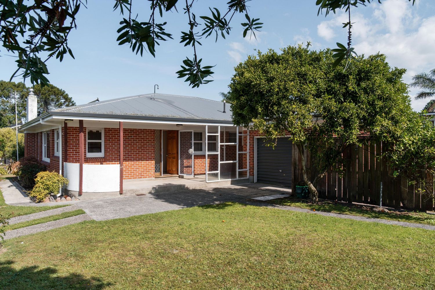 Mid-century brick home with large windows and spacious lawn surrounded by mature trees.