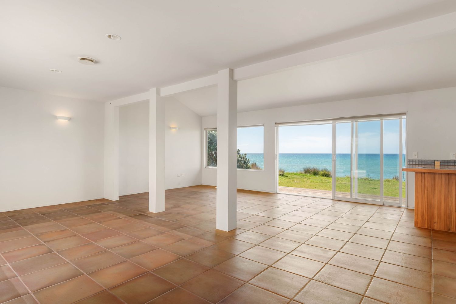 Spacious open-plan living area with terracotta tiles and white columns showcasing panoramic ocean vistas.