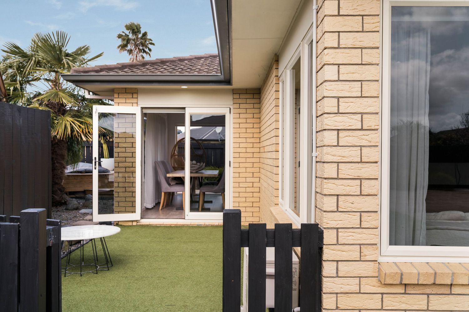 Exterior view of a cream brick house with large windows and modern black trim accents.