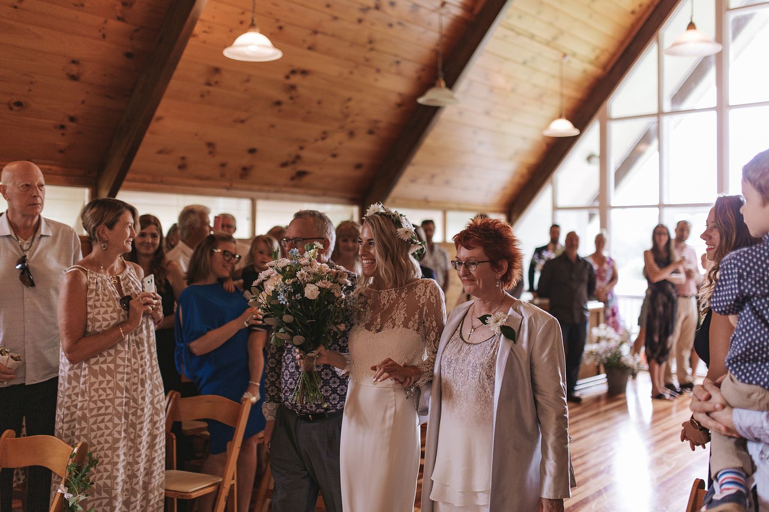Wedding guests gather inside a rustic wooden barn venue with exposed beams and natural lighting during a celebration.