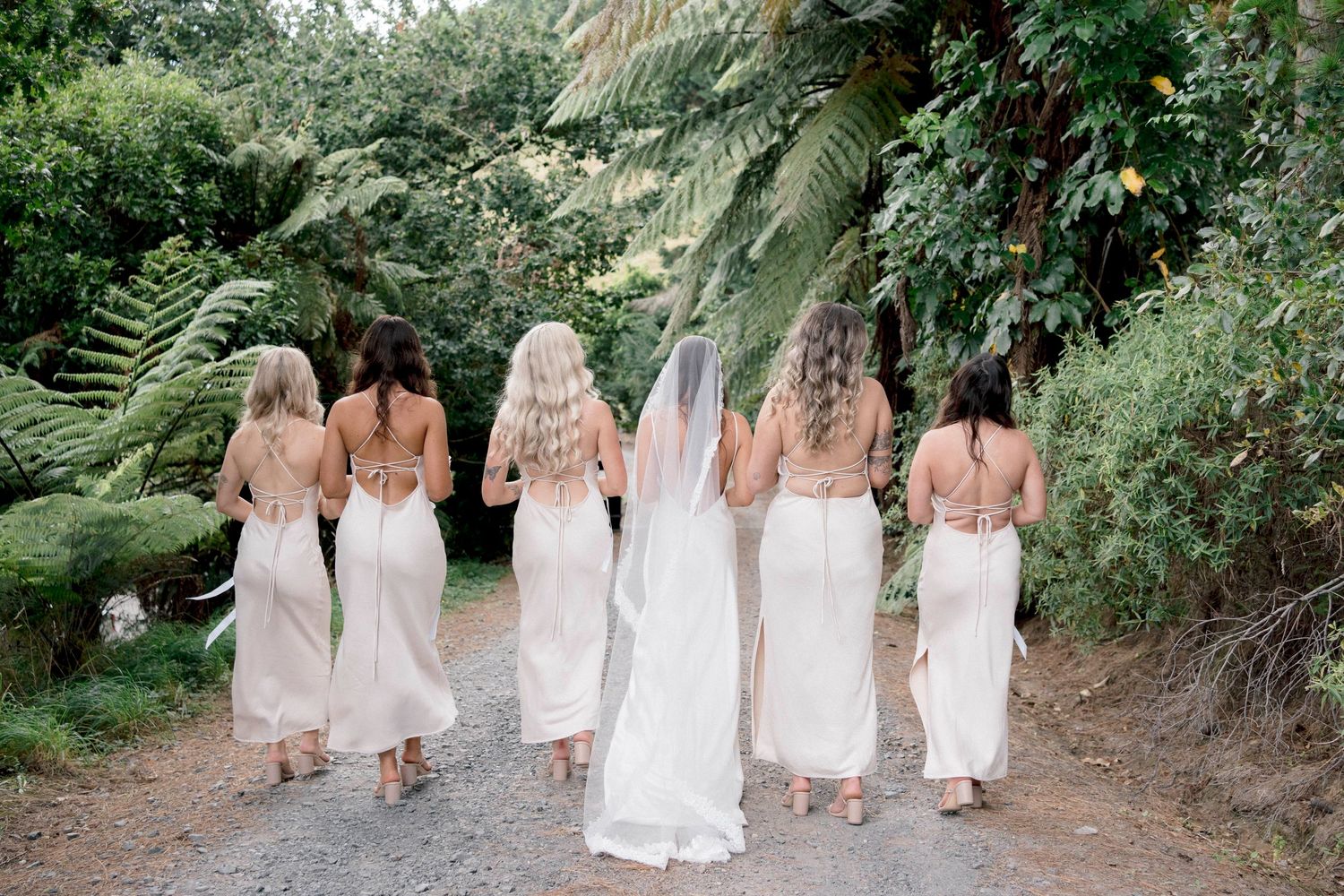 Group walks along garden path wearing matching light colored formal dresses.