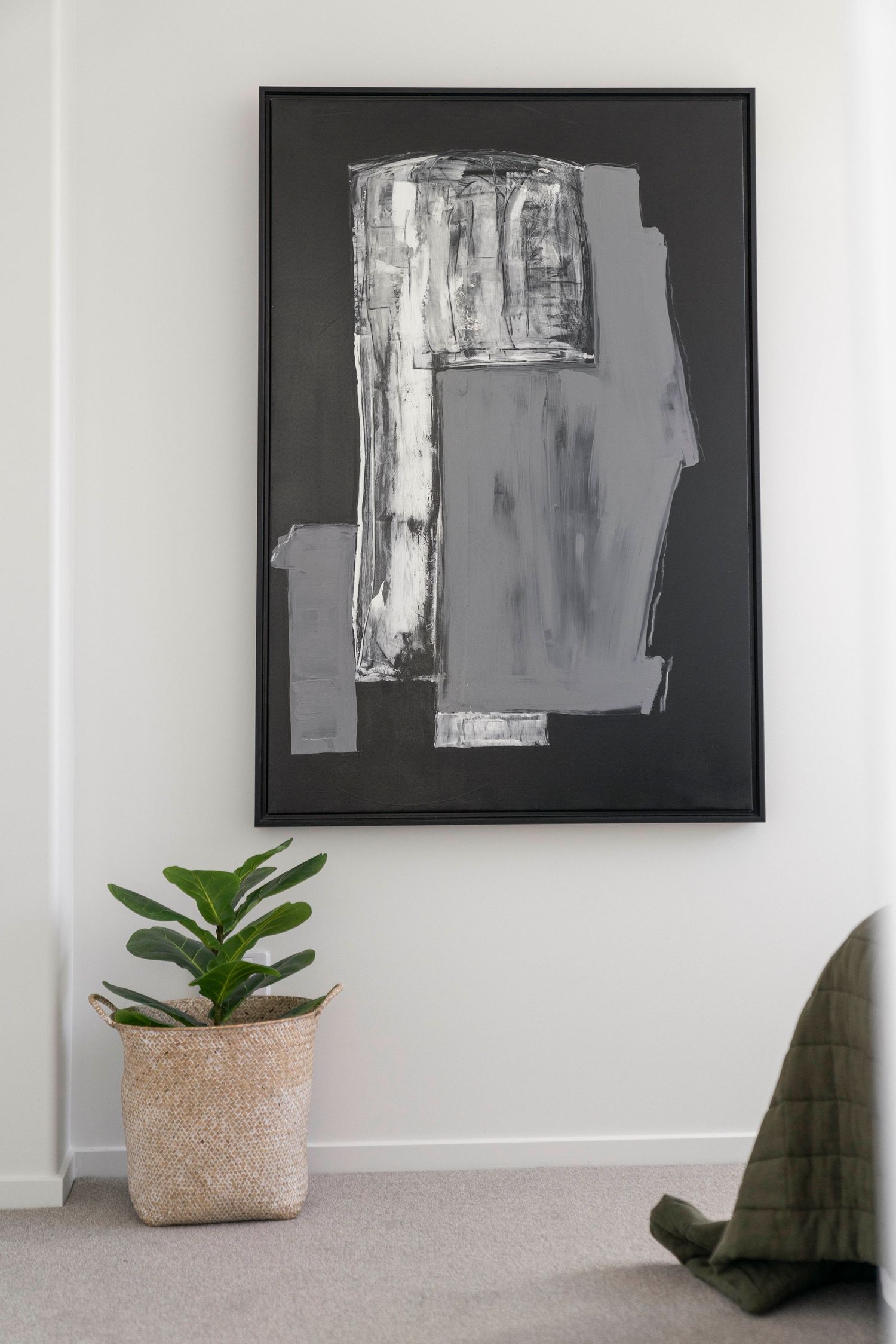 Modern abstract black and grey artwork hangs on white wall with potted plant accent.