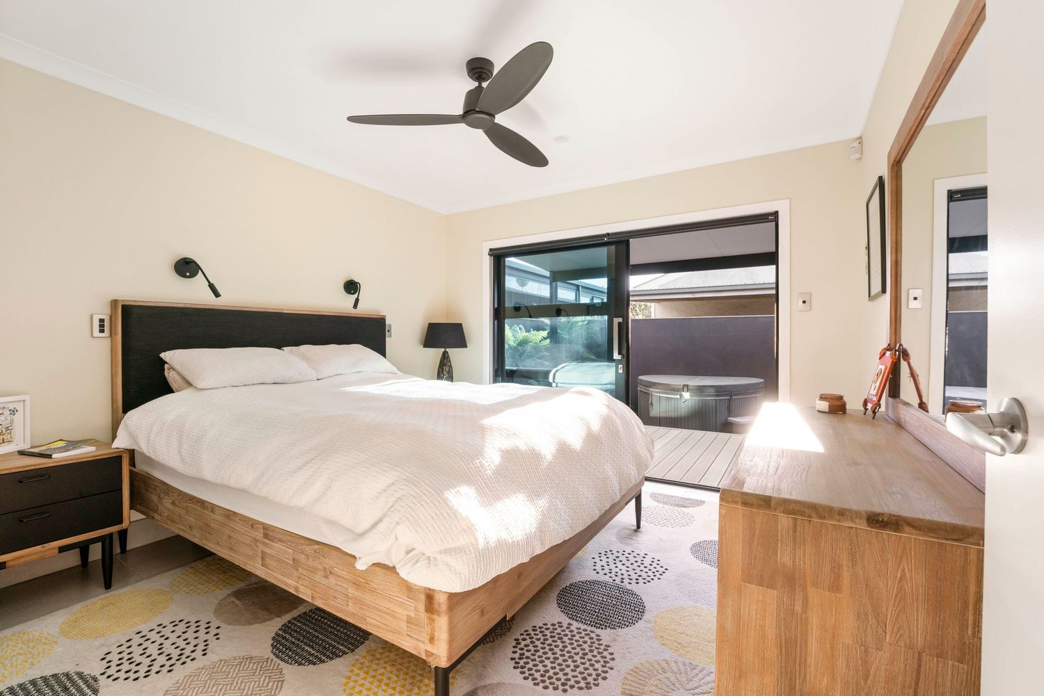 Contemporary bedroom interior with ceiling fan, wooden bed frame, and large windows letting in natural light.