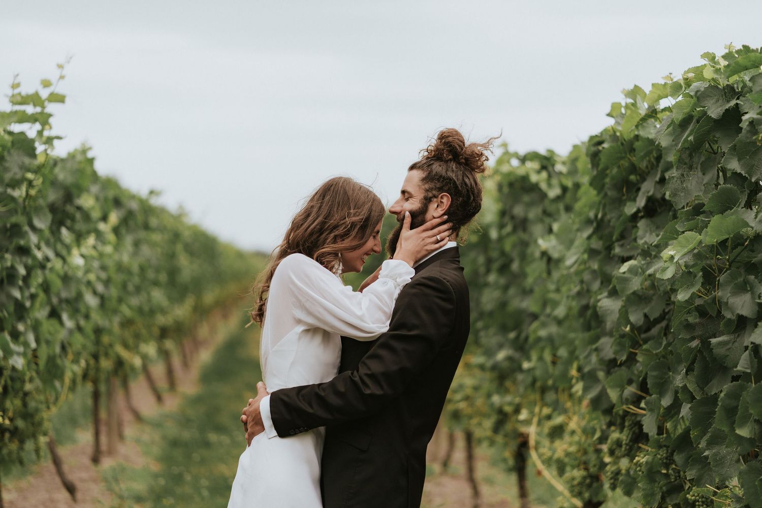 Couple sharing an intimate moment amid lush green vineyard rows in a romantic setting with natural lighting.