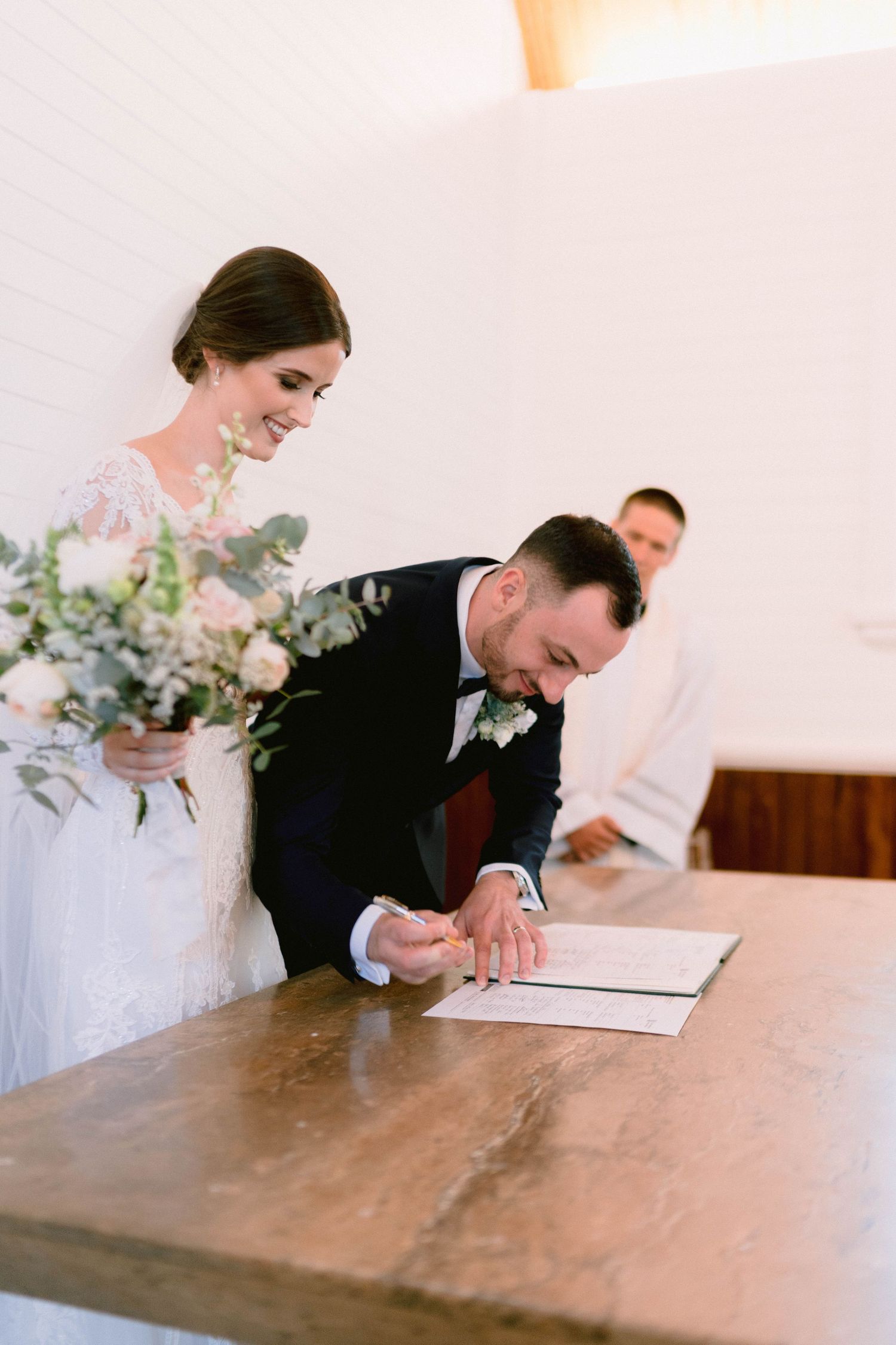 A couple signing their wedding documents at a rustic wooden table during their ceremony.