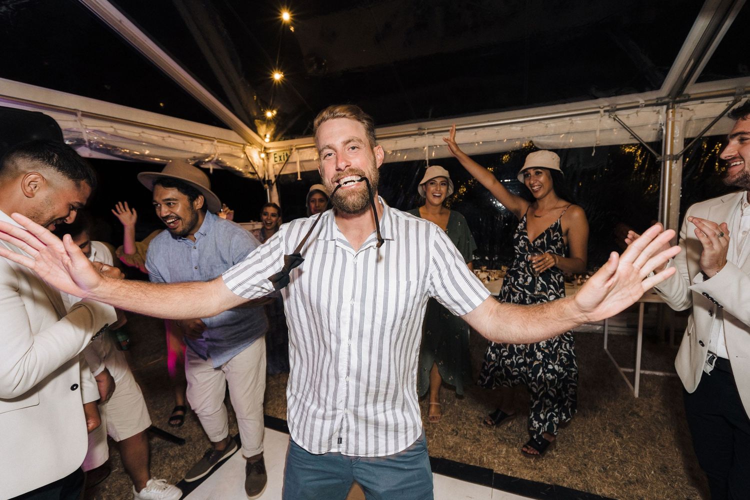 Wedding guest dances enthusiastically under tent lighting at reception celebration.