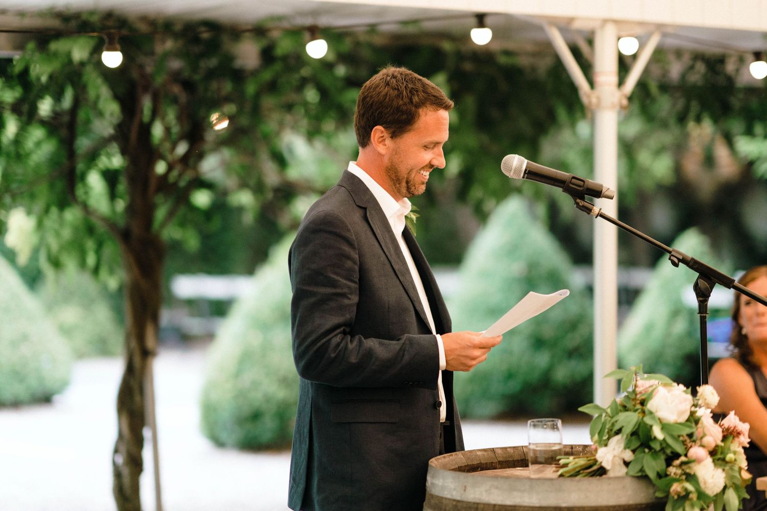 Wedding speeches being delivered at outdoor reception under white tent.