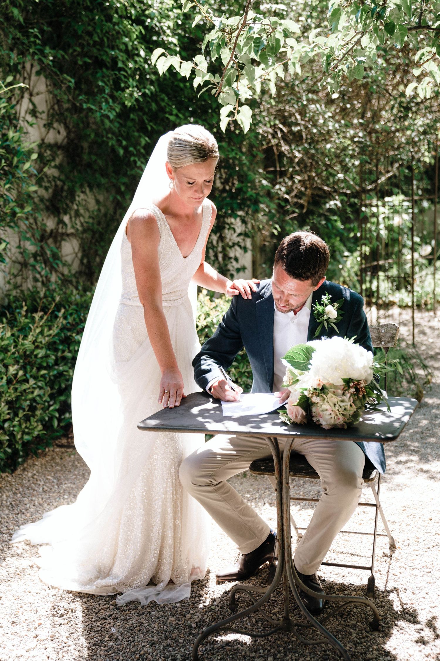 Wedding photography sequence showing signing of documents at an outdoor table in dappled sunlight.