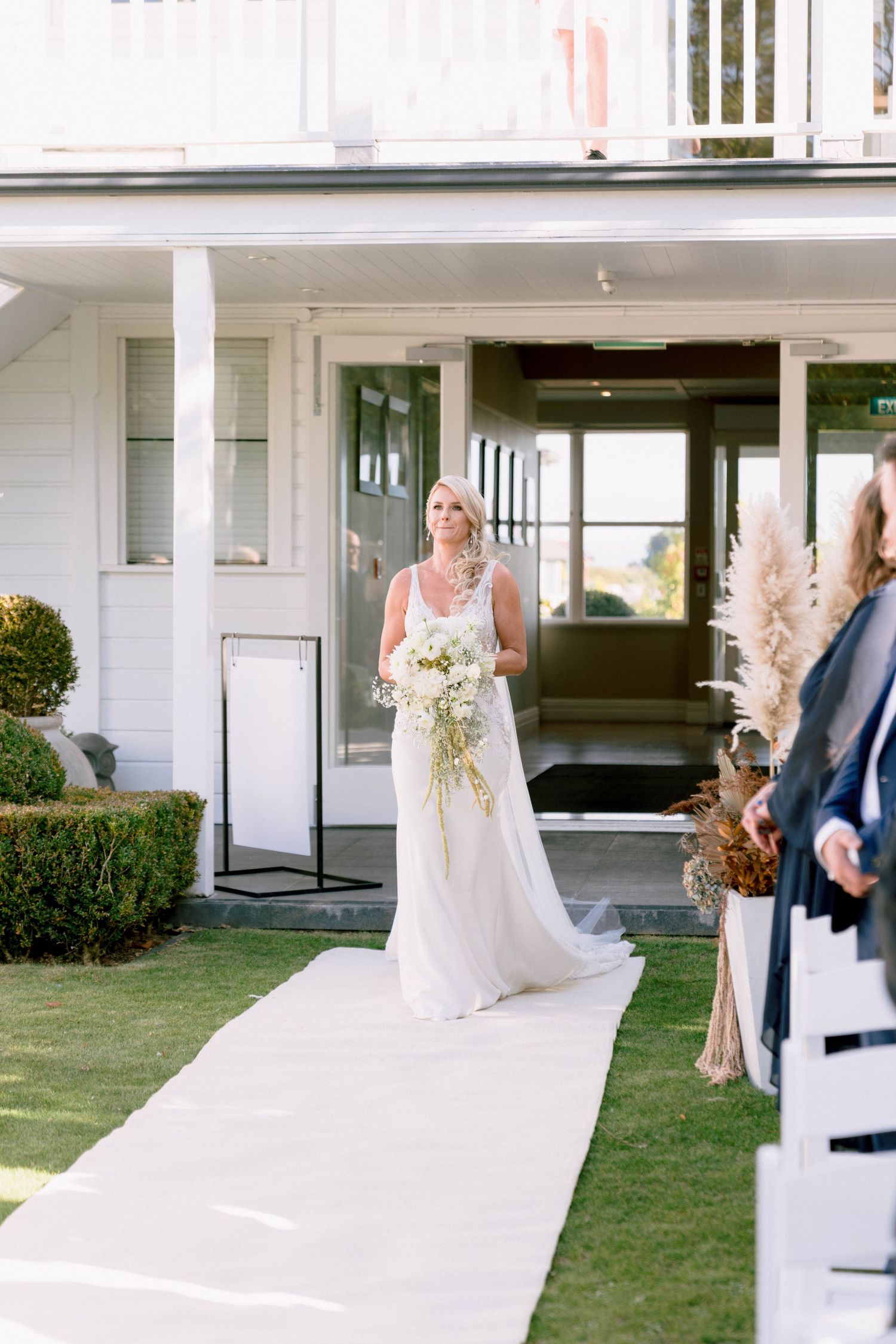 Wedding couple walks across a white aisle runner on a grassy lawn during an outdoor ceremony.
