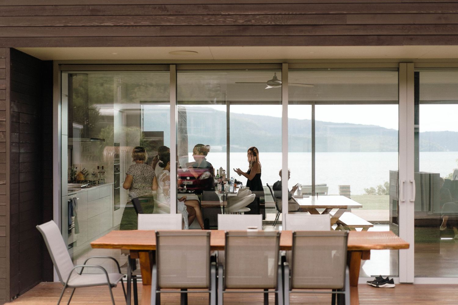 Modern dining room with large windows overlooking a waterfront view and wooden table with white chairs.
