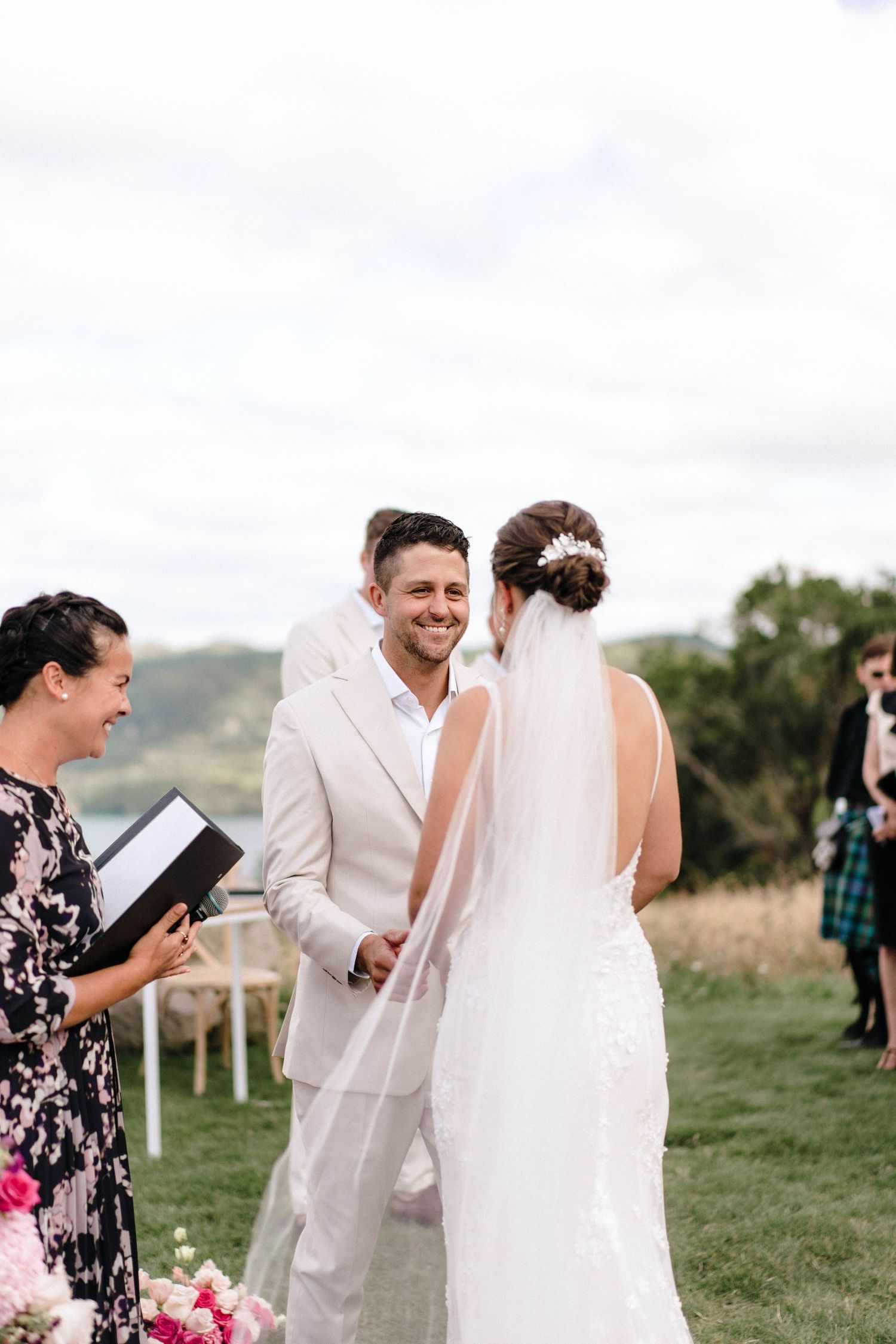 Outdoor wedding ceremony with guests in floral dresses on a sunny day.
