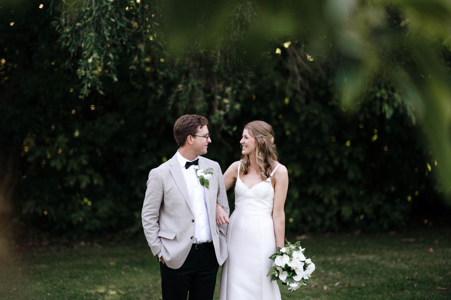 An elegant outdoor wedding photo with soft lighting and lush greenery in the background.