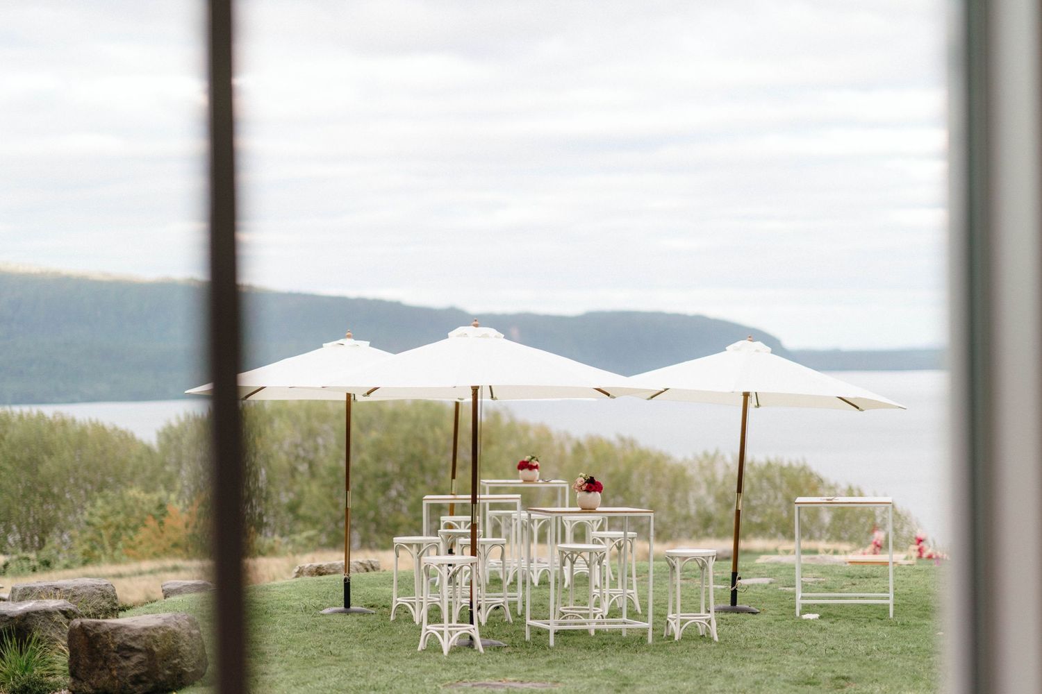 White umbrellas and cocktail tables set up on a hilltop outdoor wedding venue overlooking mountain views.