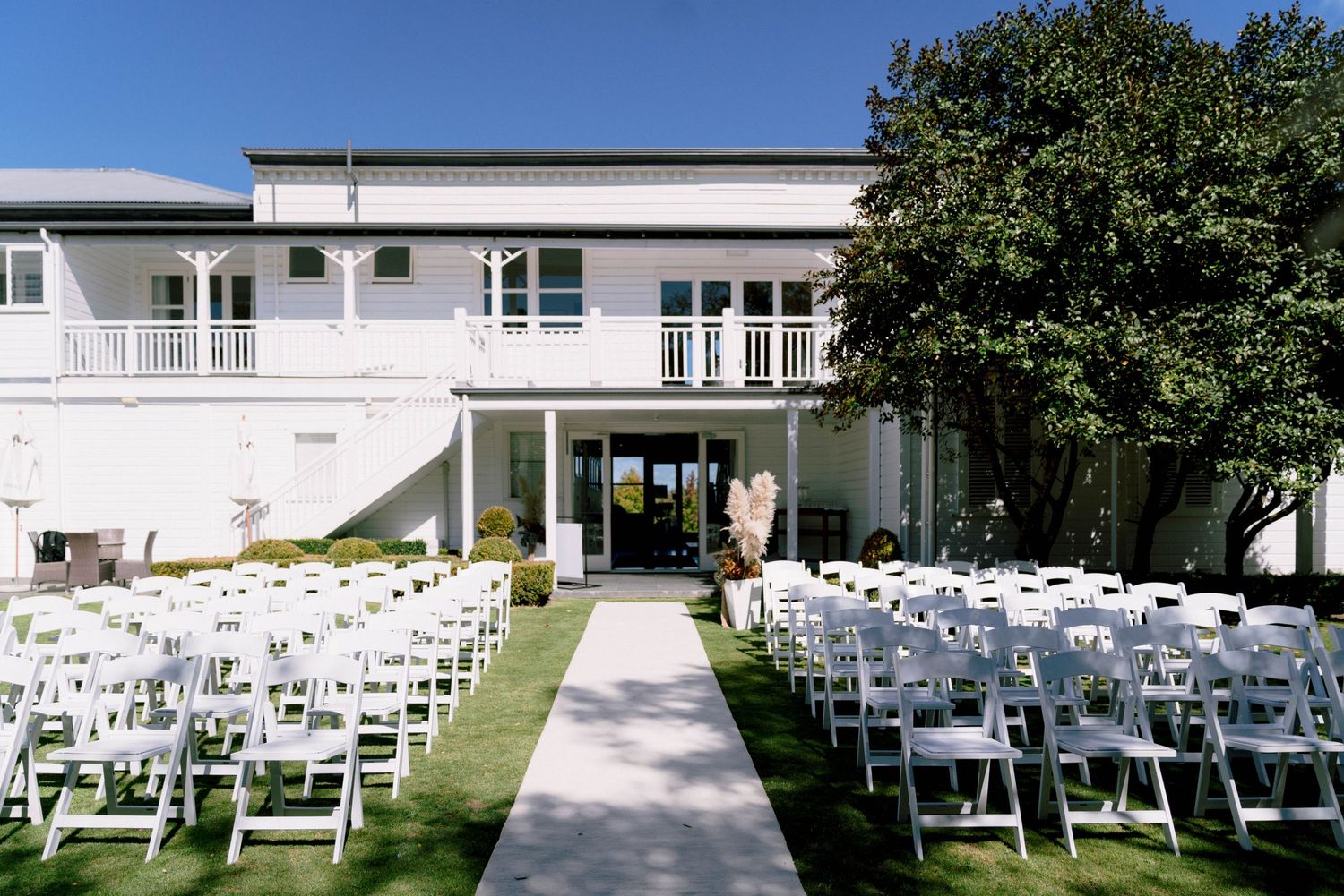 Elegant white venue with rows of chairs set up for an outdoor wedding ceremony on a manicured lawn.