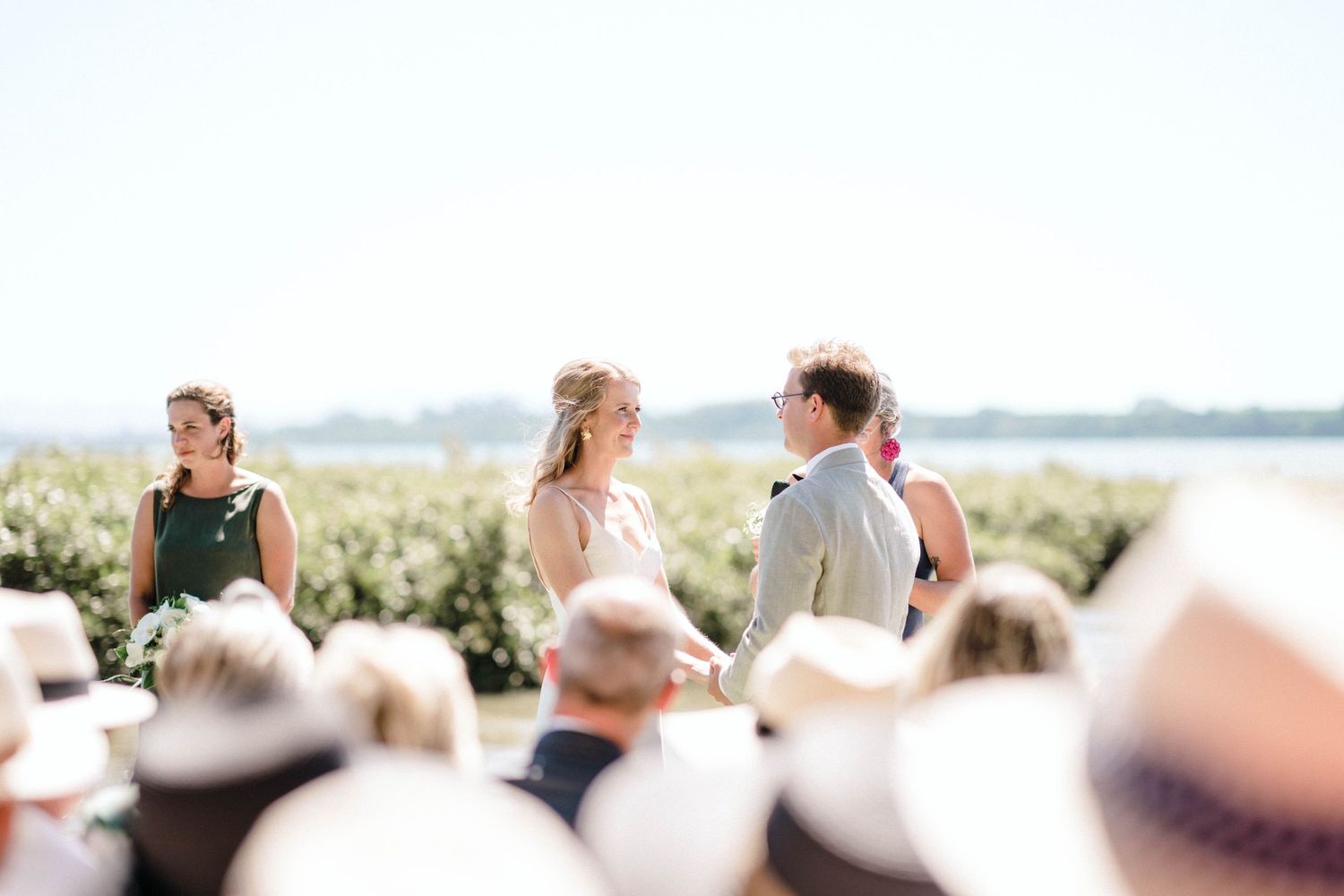 Outdoor wedding ceremony taking place near the water with guests in attendance.