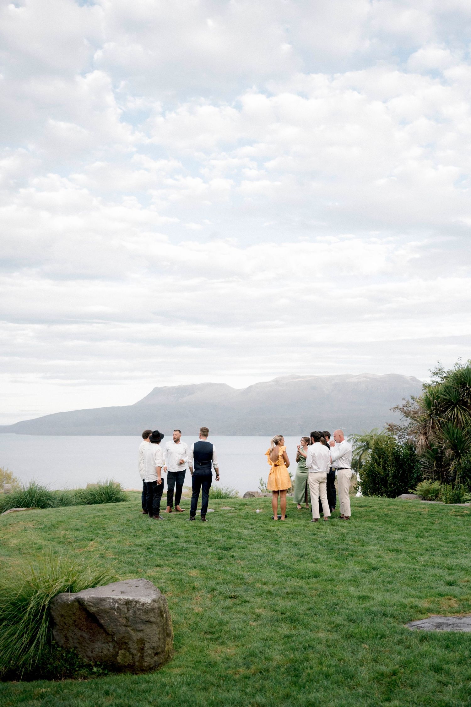 Small wedding gathering overlooking scenic mountain vista on grassy cliff.