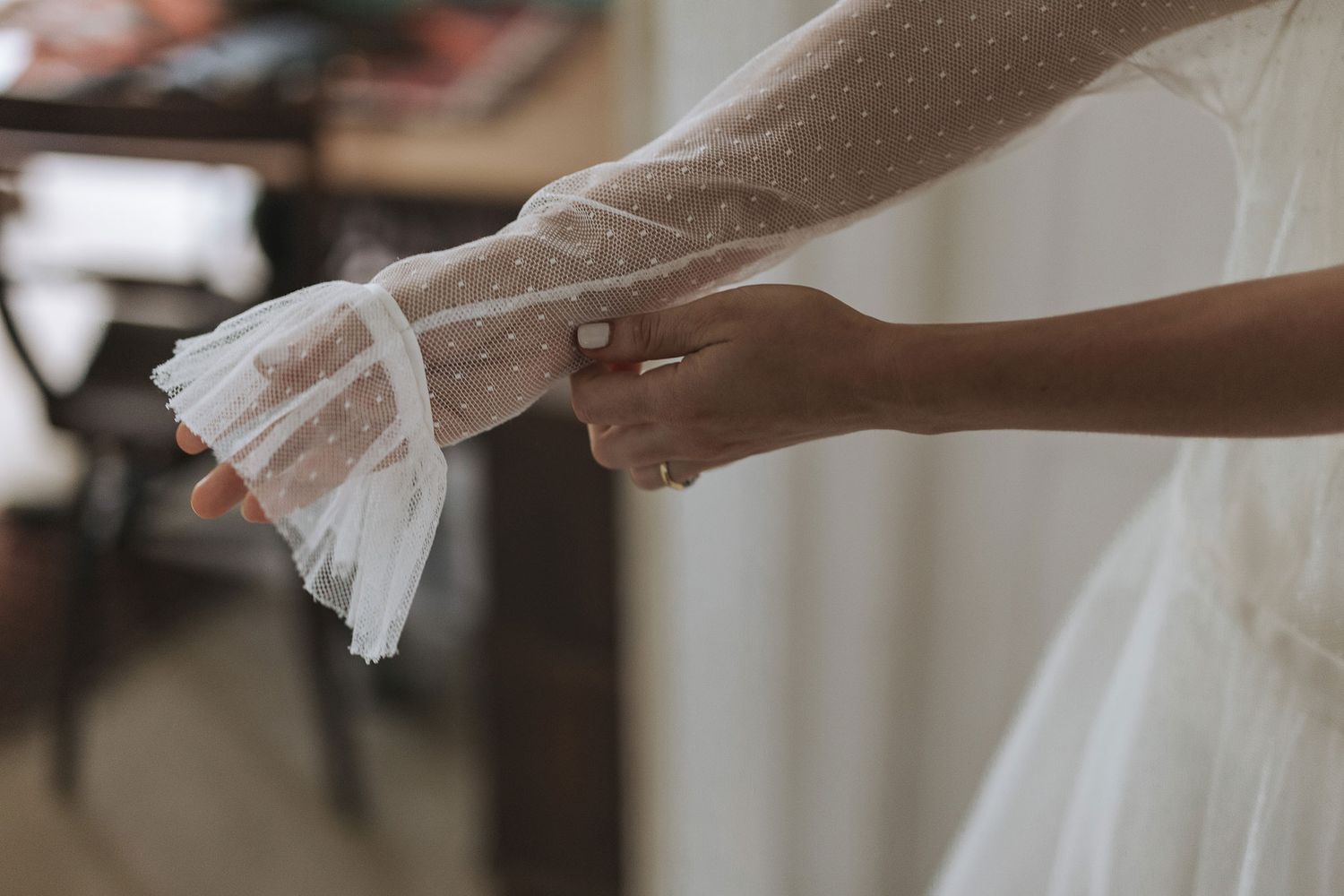 Hands carefully adjust and smooth out the delicate white fabric of a wedding dress in soft natural lighting.
