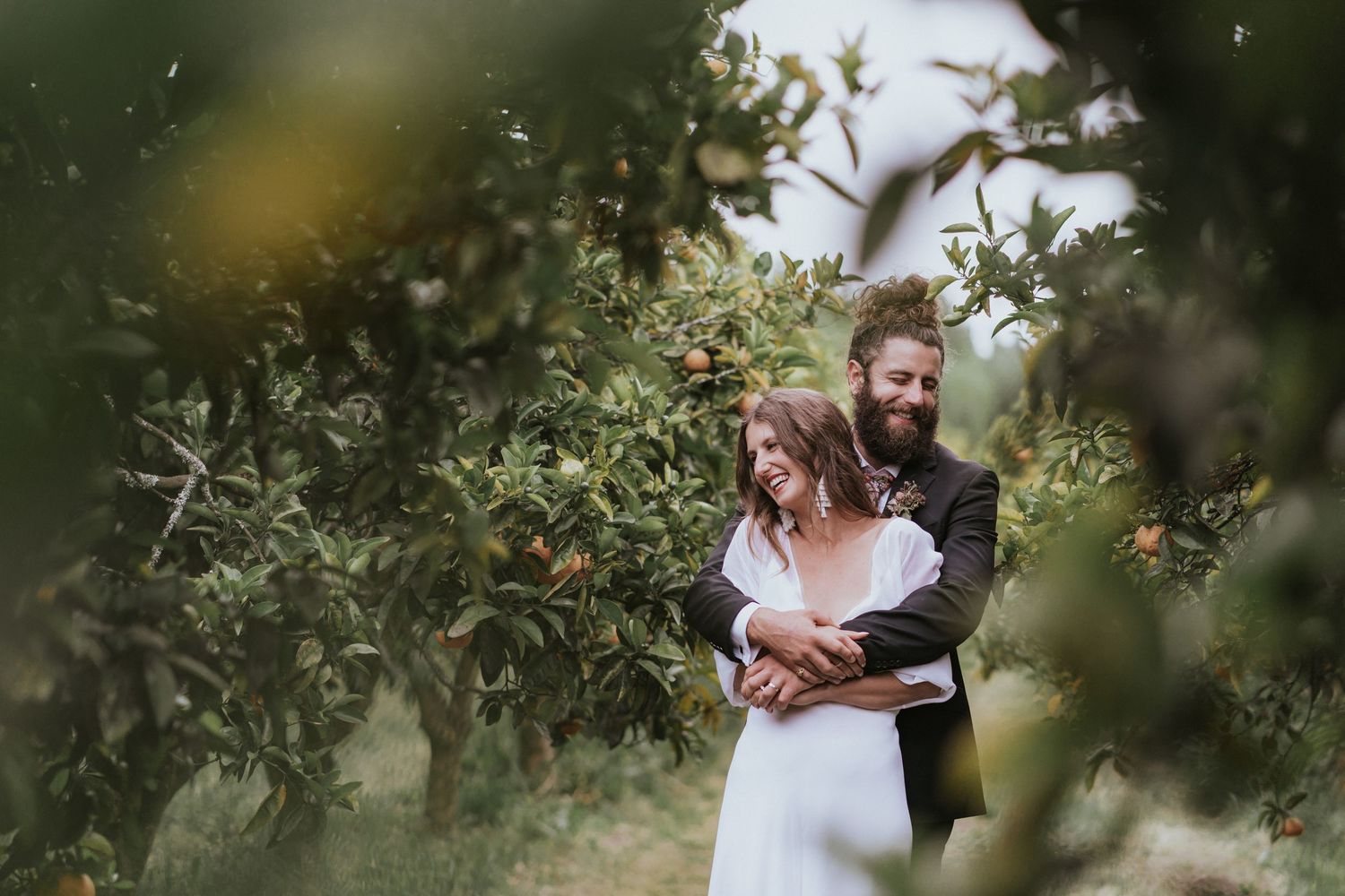 White-clad couple embraces tenderly in a verdant citrus grove during an intimate outdoor photoshoot.