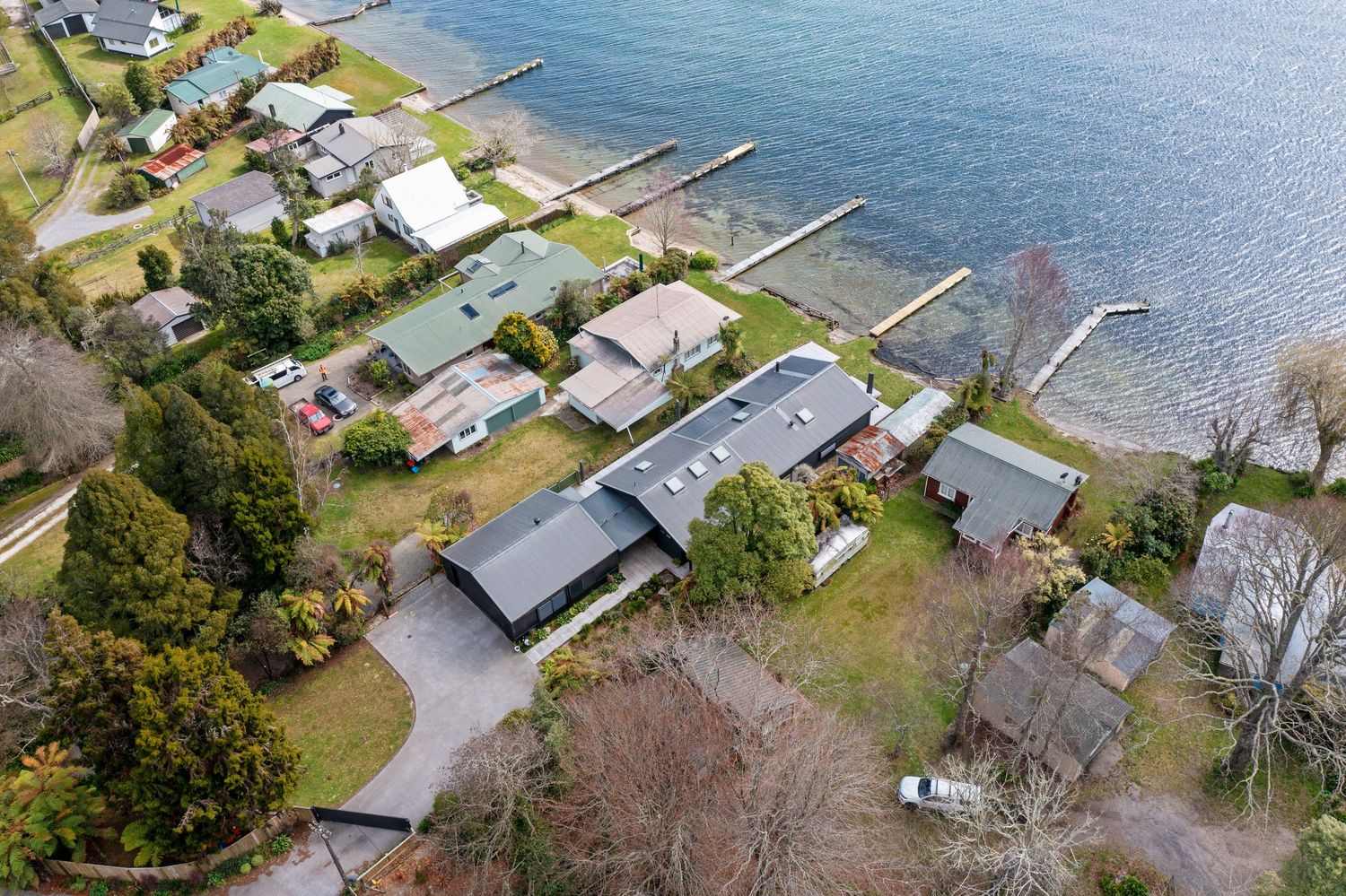 Aerial view of waterfront homes with private docks extending into a calm blue bay on a sunny day.