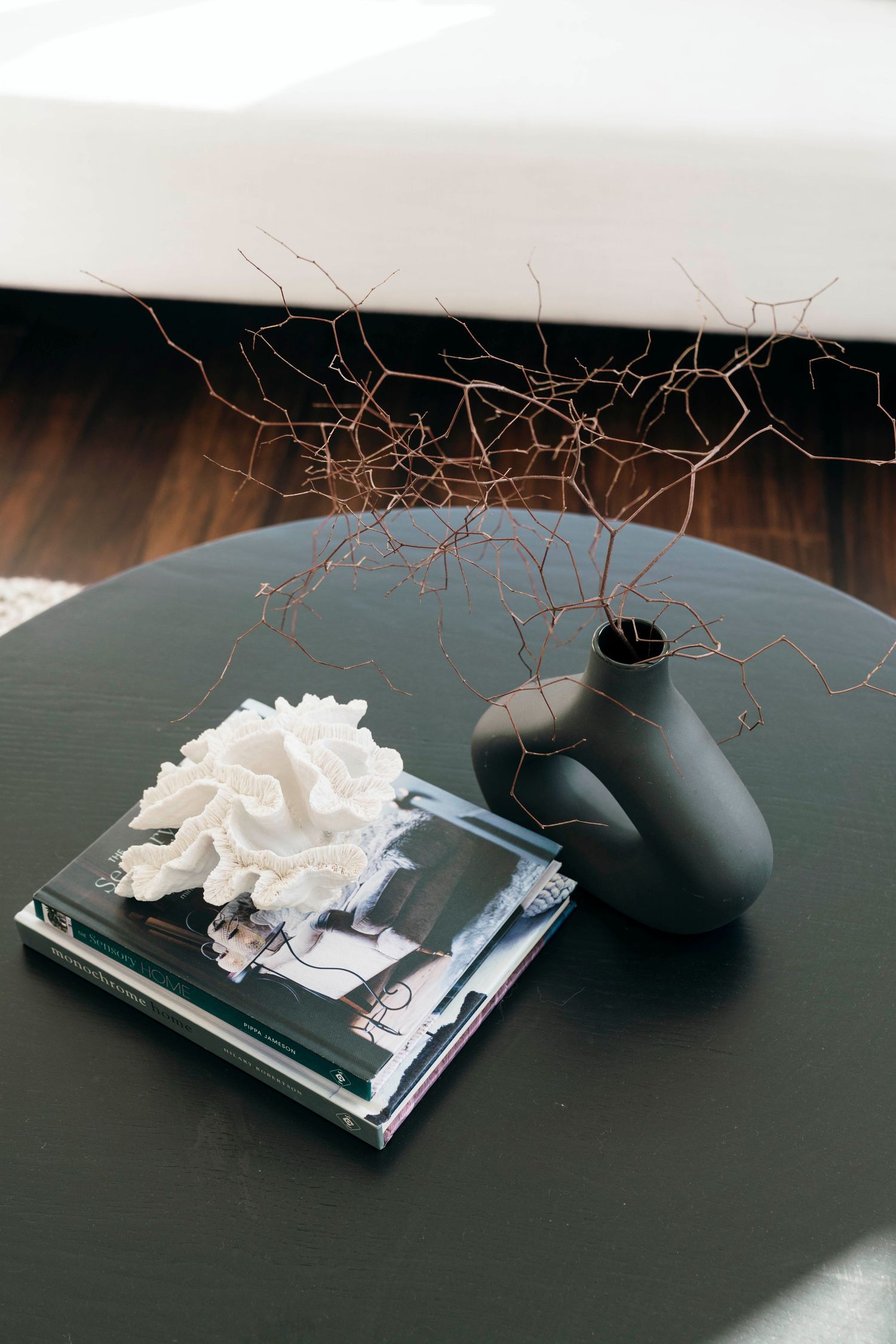 Modern black coffee table with stacked books, white coral decor, and black vase with dried branches.