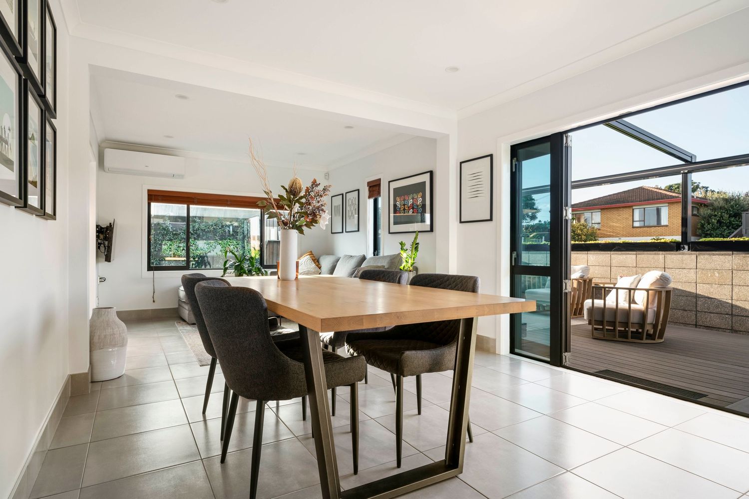 Modern dining room with wooden table, black chairs and glass sliding doors leading to outdoor deck.
