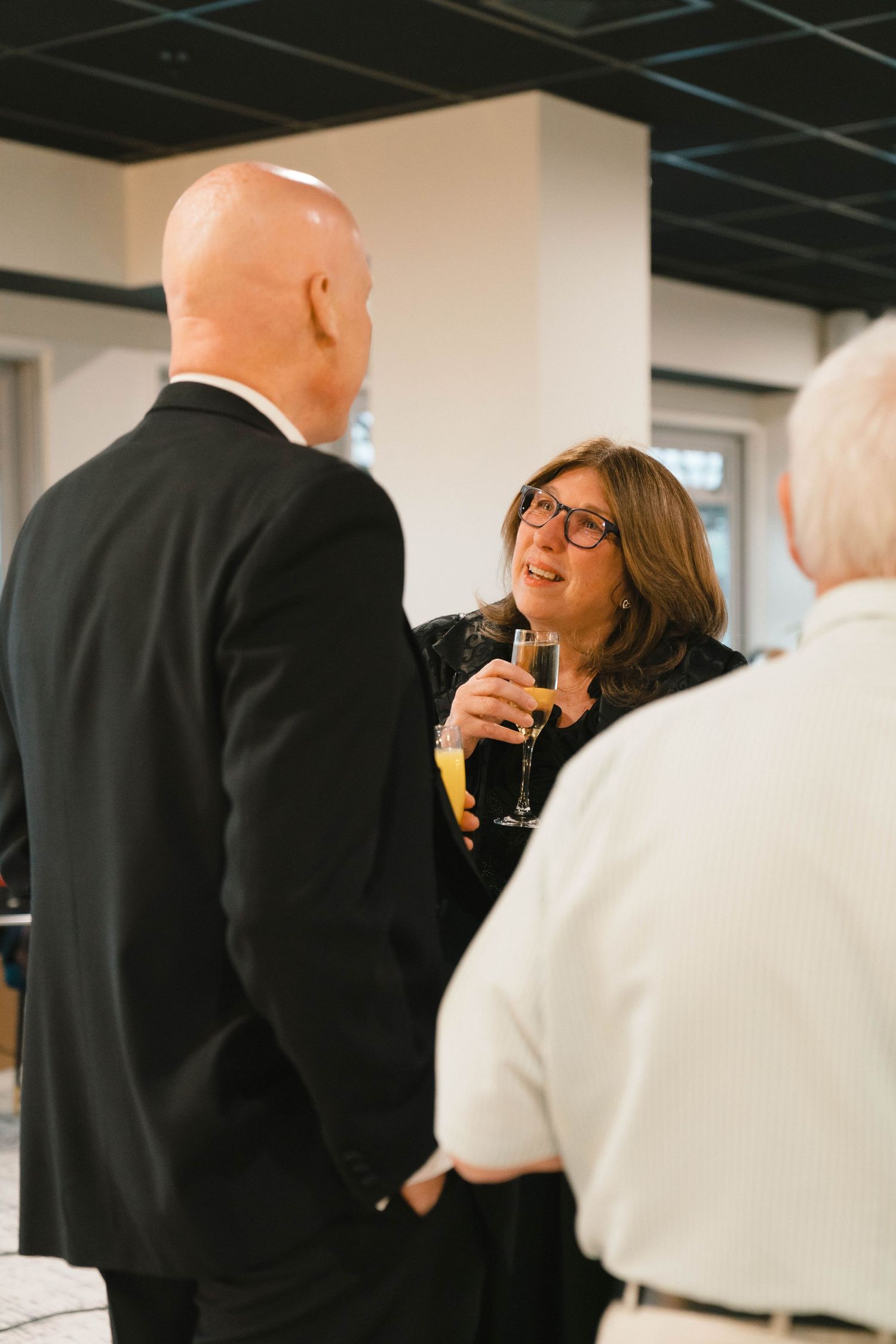 People in formal attire socializing at an indoor event with dark ceiling.