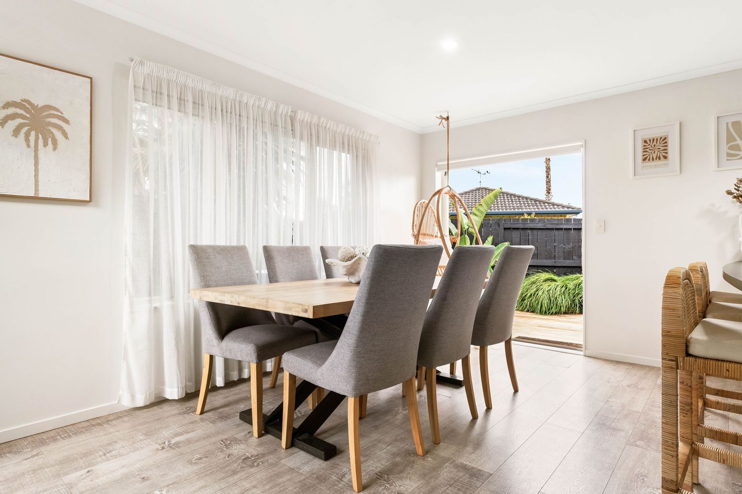 Modern dining area with white walls, grey upholstered chairs, and wooden furniture in an open plan layout.