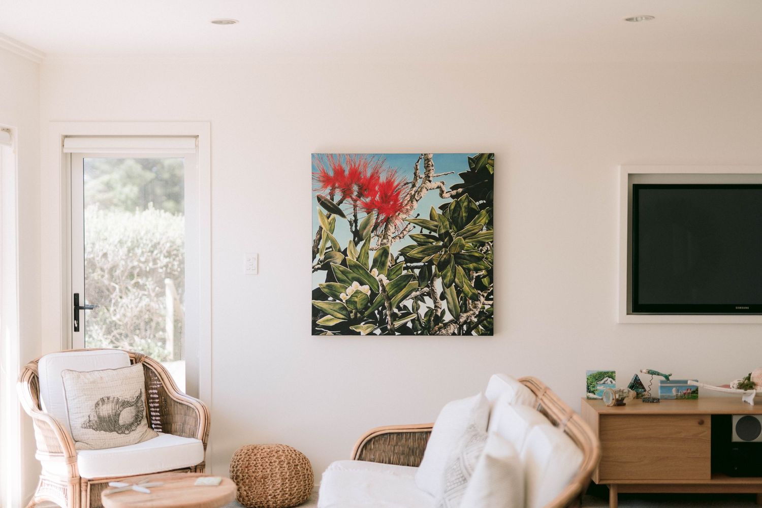 Modern living room interior with vibrant red floral artwork, rattan chair, and wall-mounted TV above wooden console.