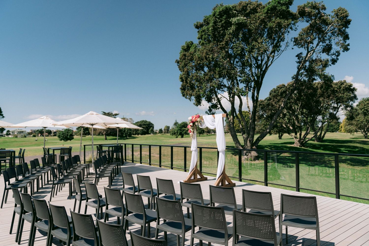 An outdoor wedding ceremony setup in a garden with rows of white chairs facing a scenic view of lush greenery and mountains.