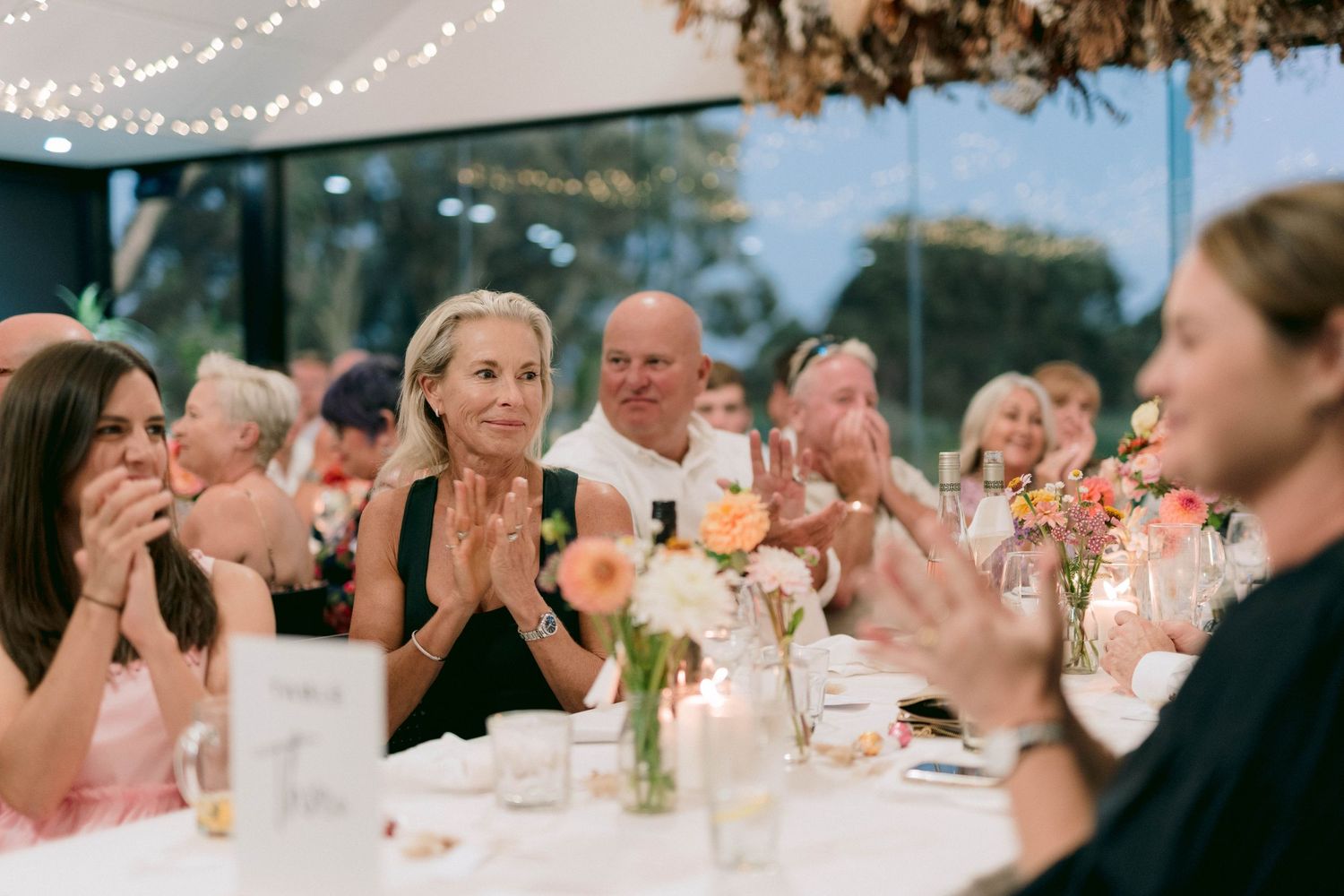 Wedding guests seated at outdoor reception tables share joyful laughter during evening celebration.