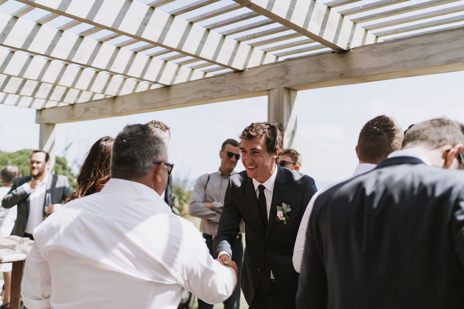 A group gathers under a wooden pergola during what appears to be an outdoor event or celebration.