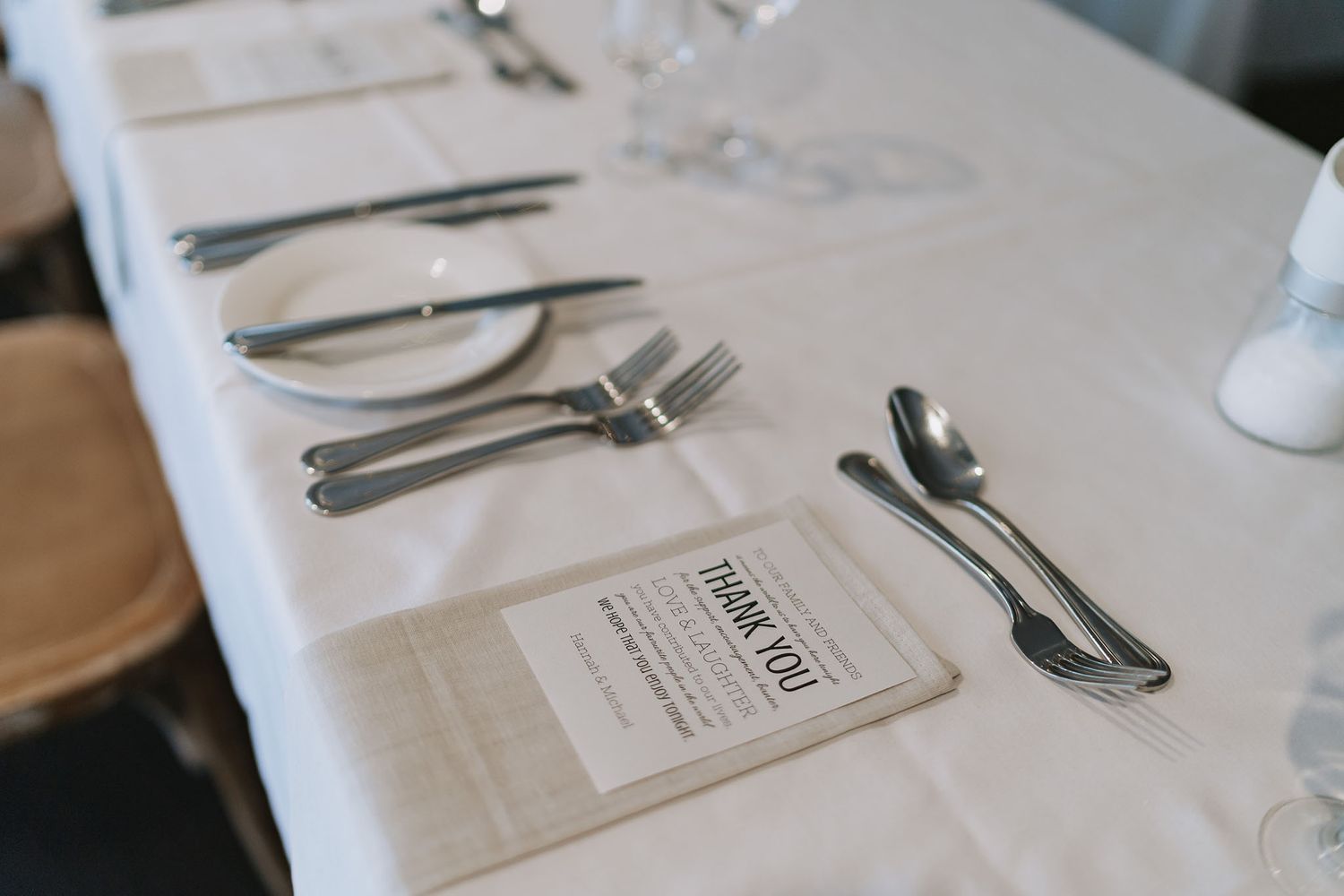 Place setting at an elegant table with silverware, white tablecloth and menu card.