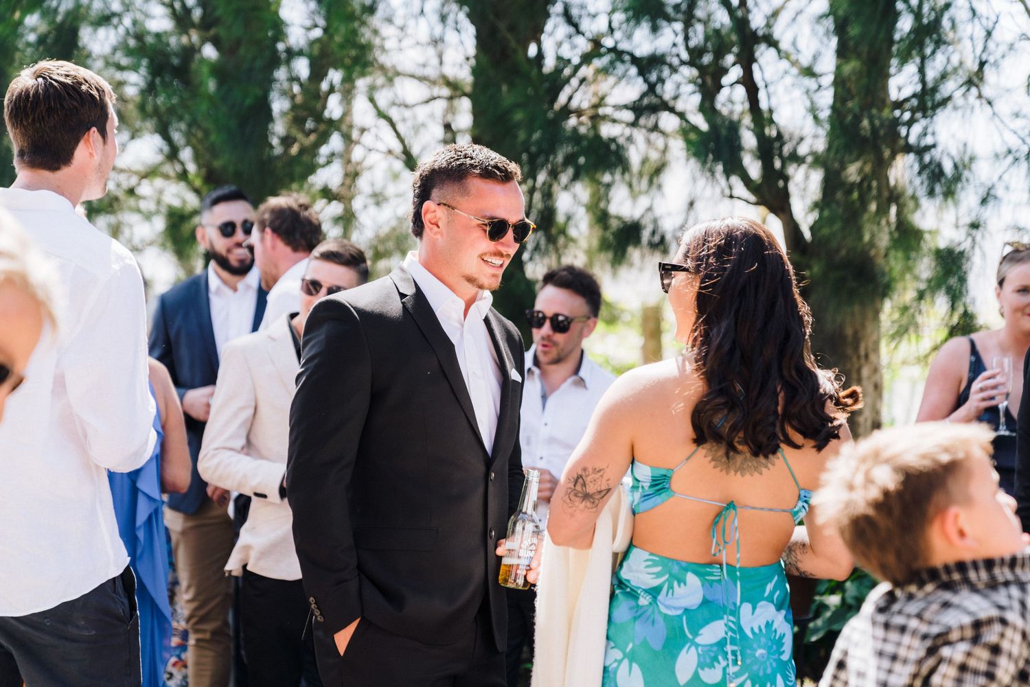 Wedding guests mingle and socialize at an outdoor reception party on a sunny afternoon.