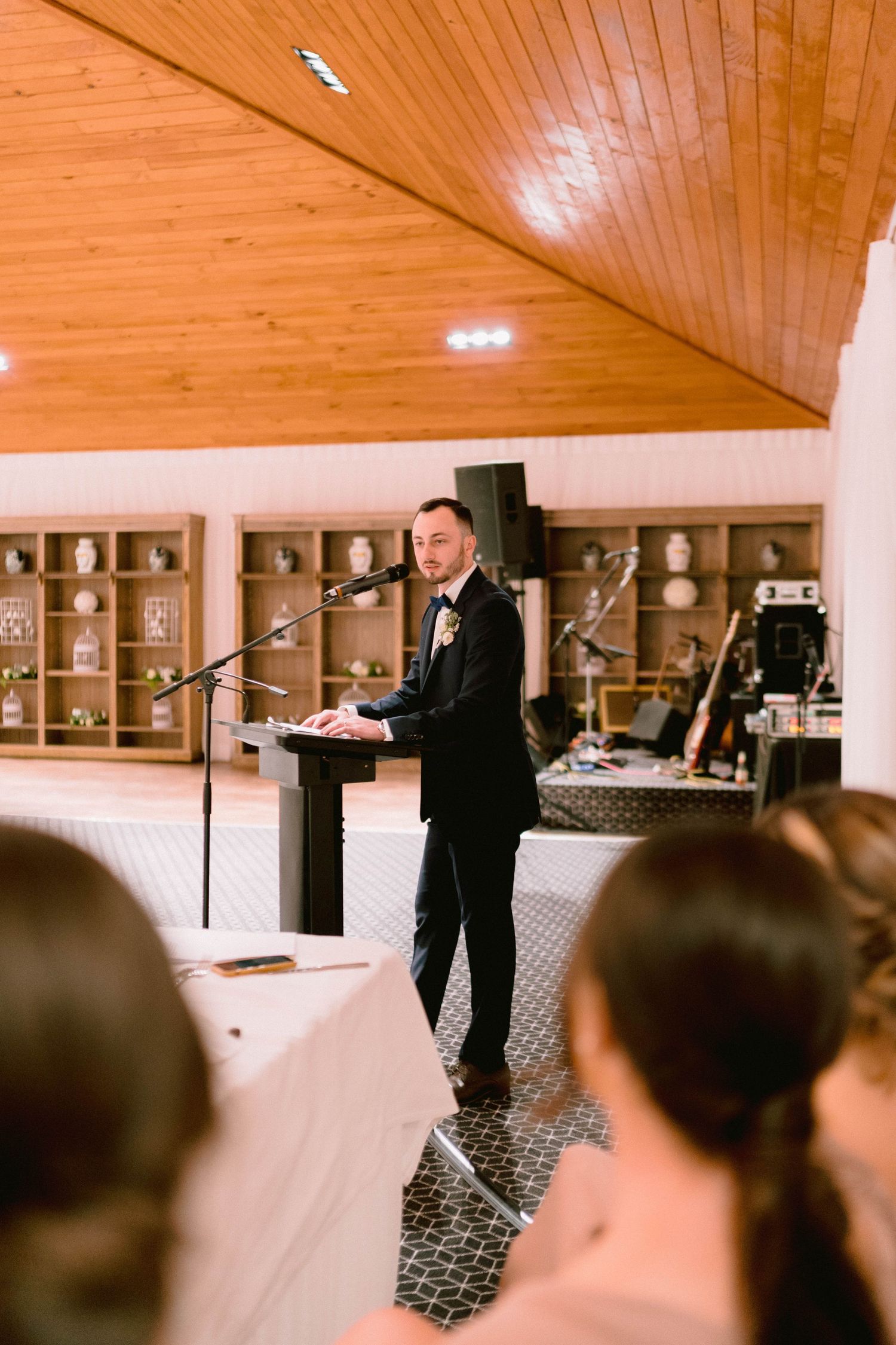 A speech being given during a wedding reception in a wood-paneled room with decorative shelving.