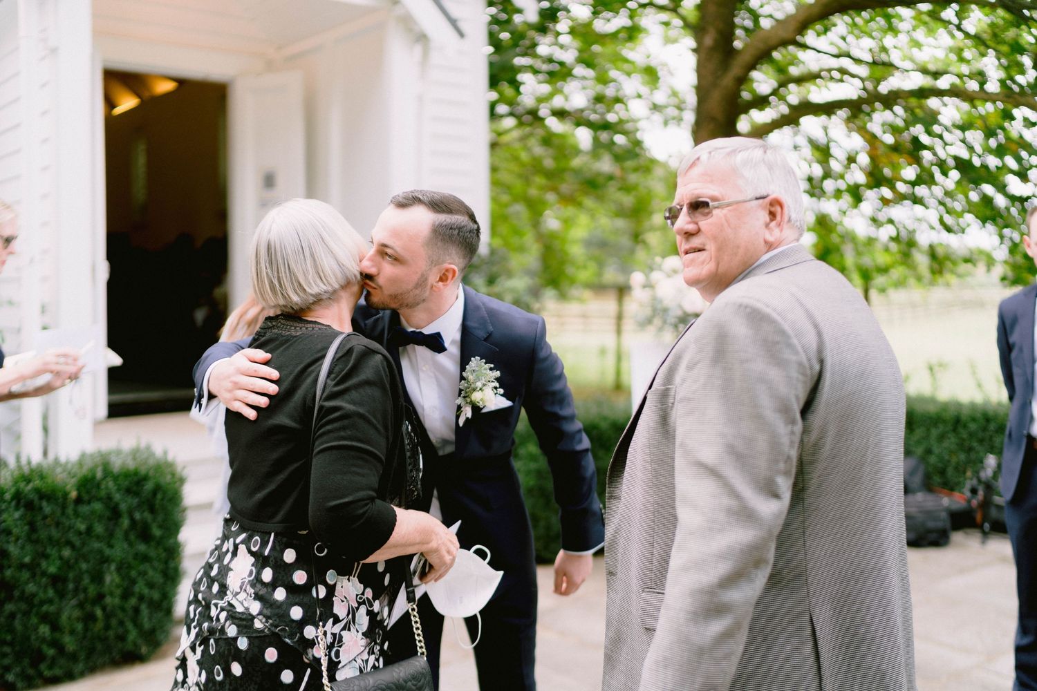 Wedding guests share warm greetings and embraces outside a venue on a lovely spring day.