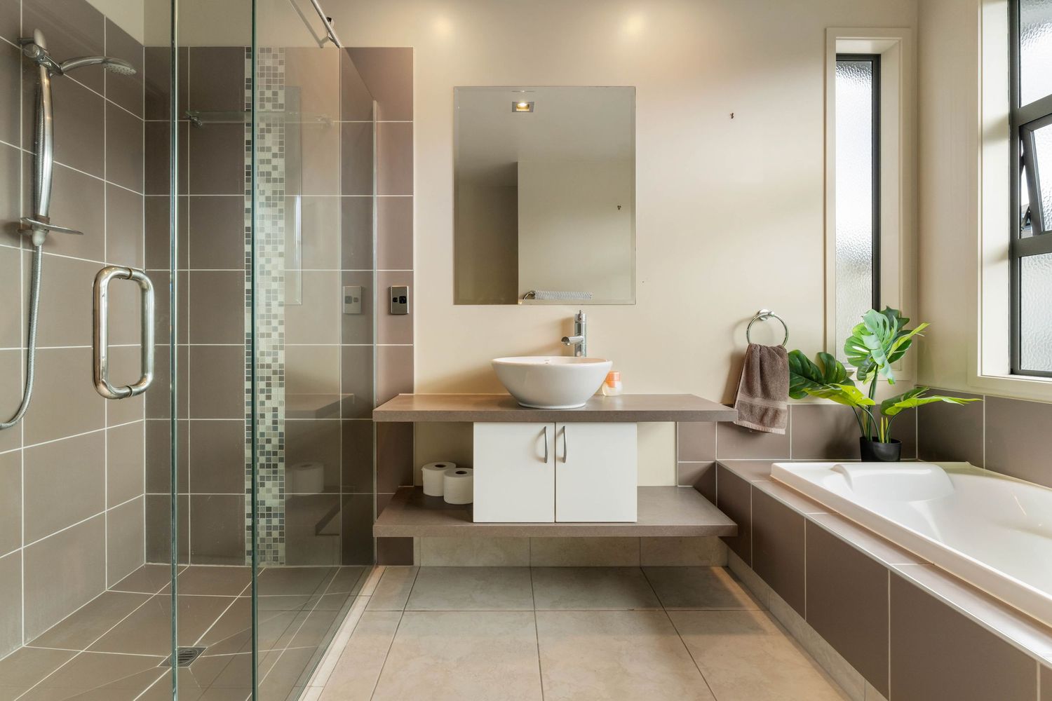 Sleek modern bathroom with glass shower enclosure, brown tiles and minimalist fixtures.