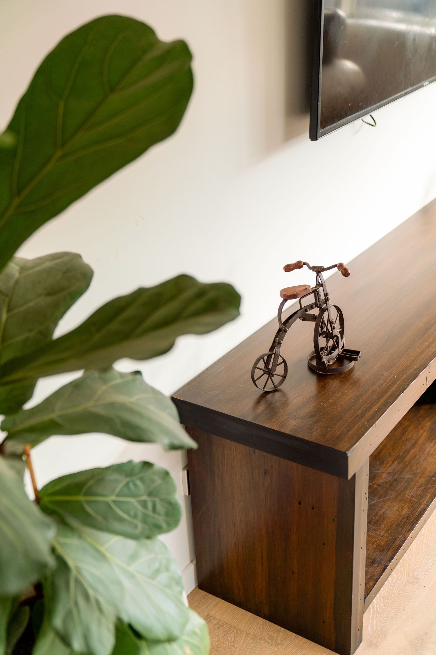 Decorative metal bicycle sculpture displayed on wooden console table with fiddle leaf fig plant in foreground.