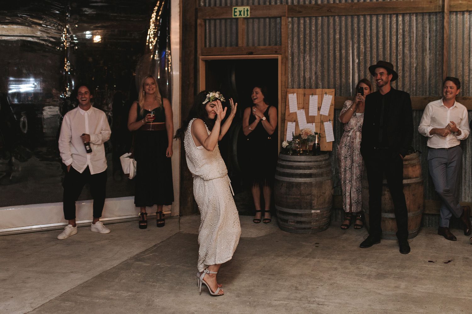 A couple dances together during their wedding celebration while guests watch from the sides of the rustic venue.