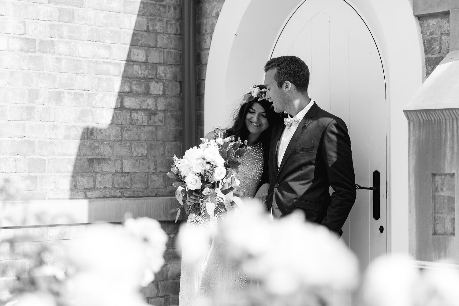 Romantic black and white wedding portrait by arched church doorway with bridal bouquet.