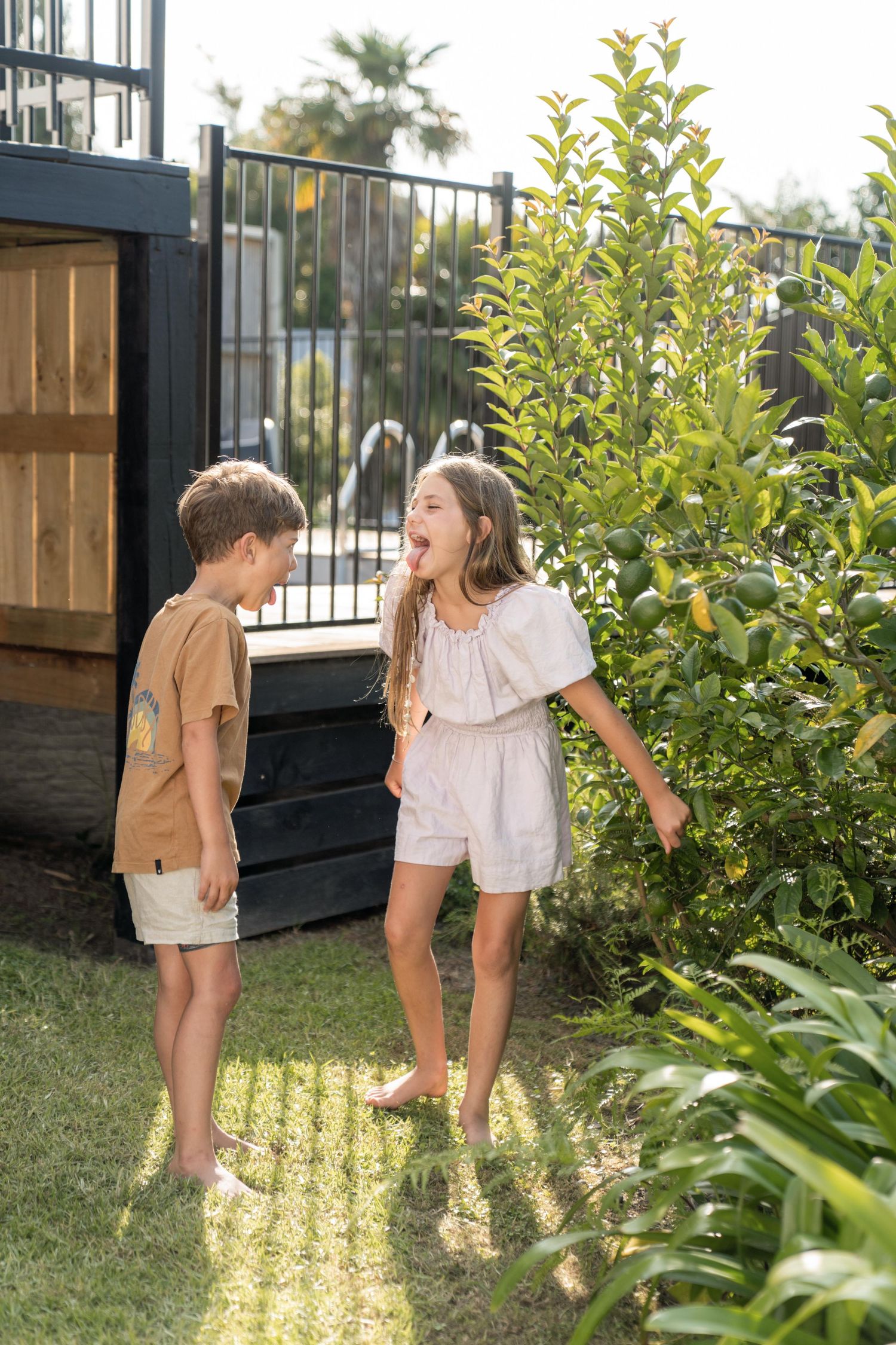 Two children laughing and playing in a sunny garden with lush greenery.